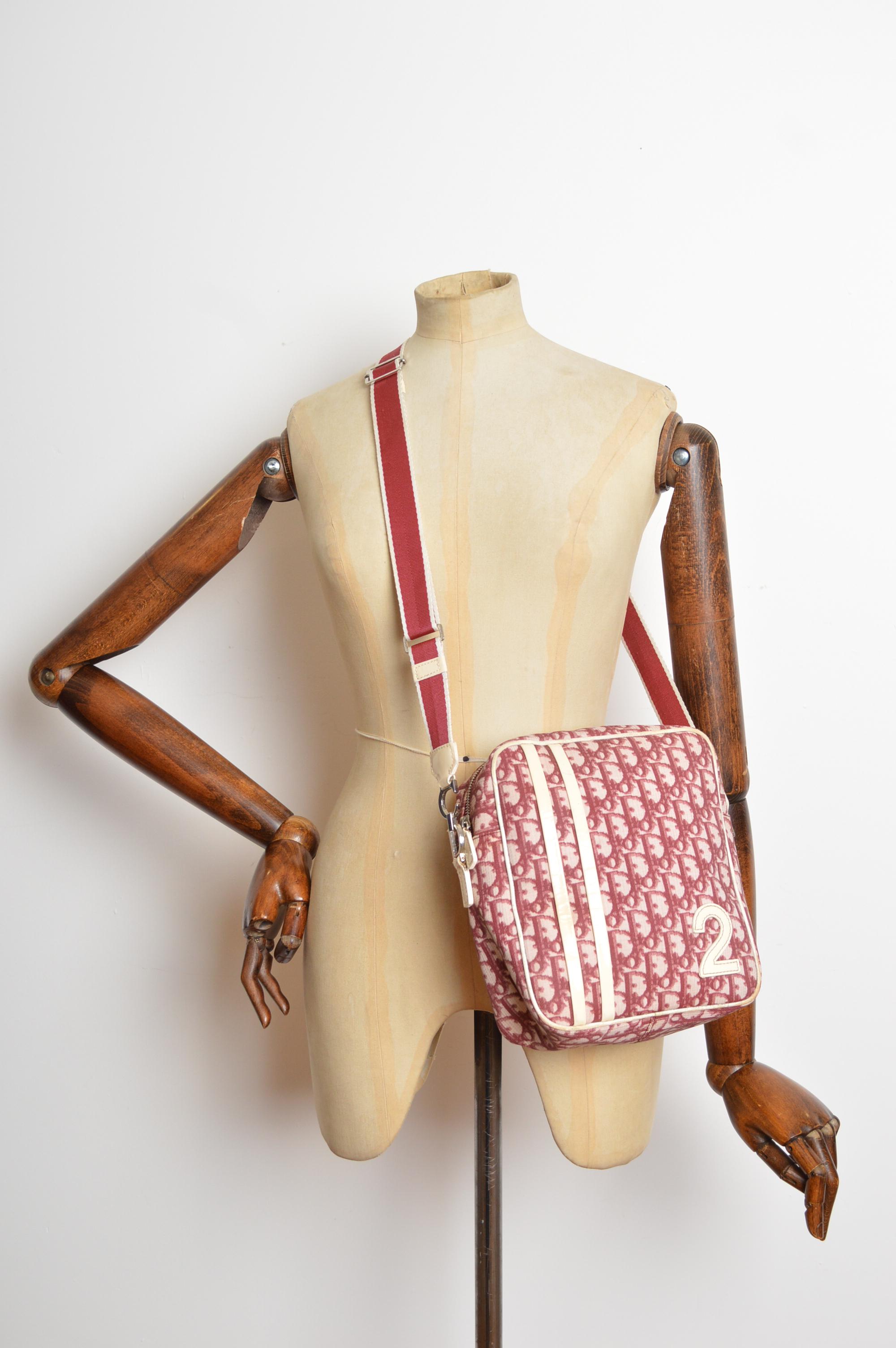 Una borsa laterale trotter color lampone di John Galliano for Christian Dior degli anni 2000. Presenta una tracolla completamente regolabile, una chiusura a zip, un ulteriore scomparto interno con zip e hardware C.A.D. cromato. 
Le misure sono