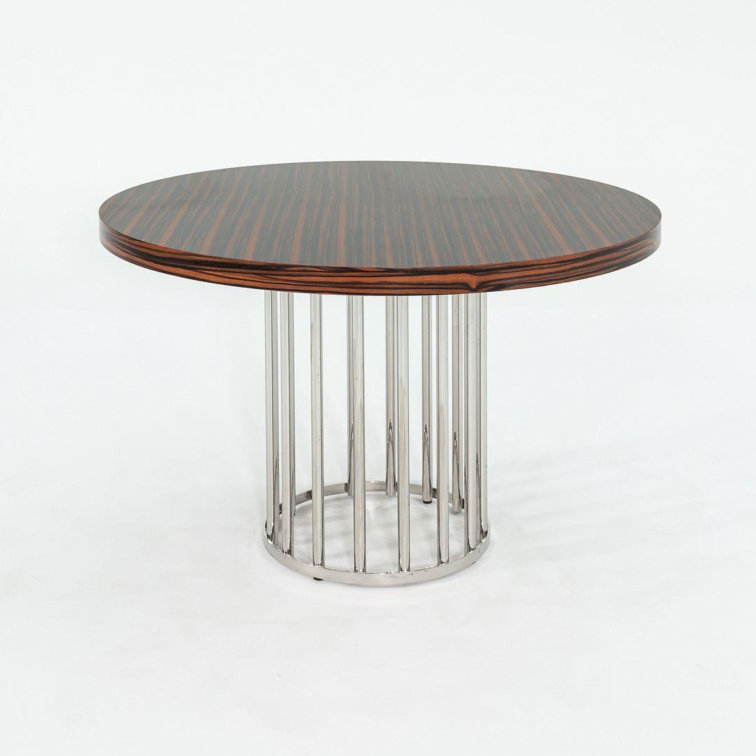 This is a custom-designed round dining table with a Macassar Ebony top and a highly polished stainless steel base. It has Art Deco lines, with round polished steel rods welded to flat steel rims. The piece is substantial, with the wooden veneer top