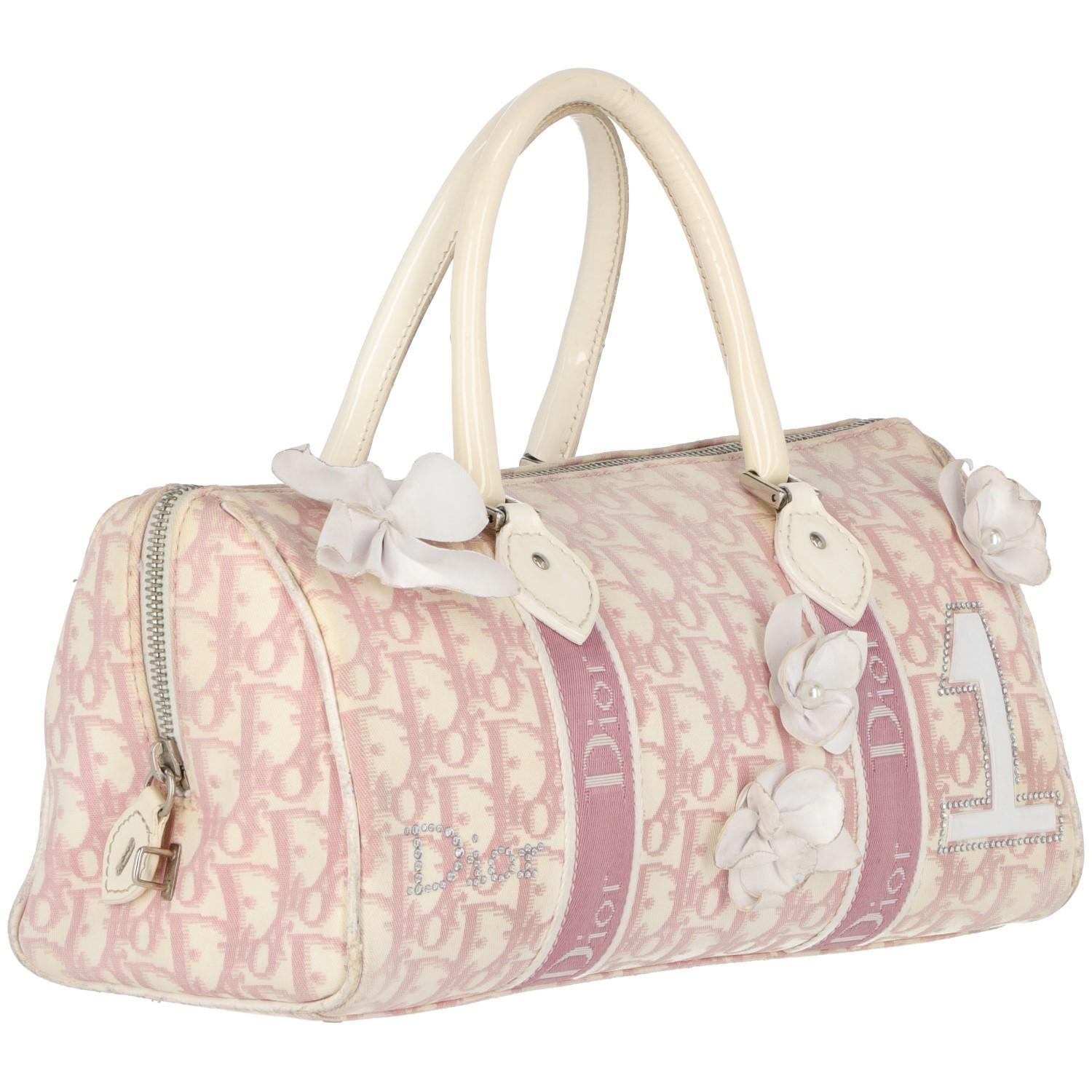 The lovely Dior handbag is made in Italy, with pink monogram branded on white nylon fabrics. It features two decorative pink/white vertical branded bands, two rhinestone elements and white patent applied flowers on the front. With white shiny patent