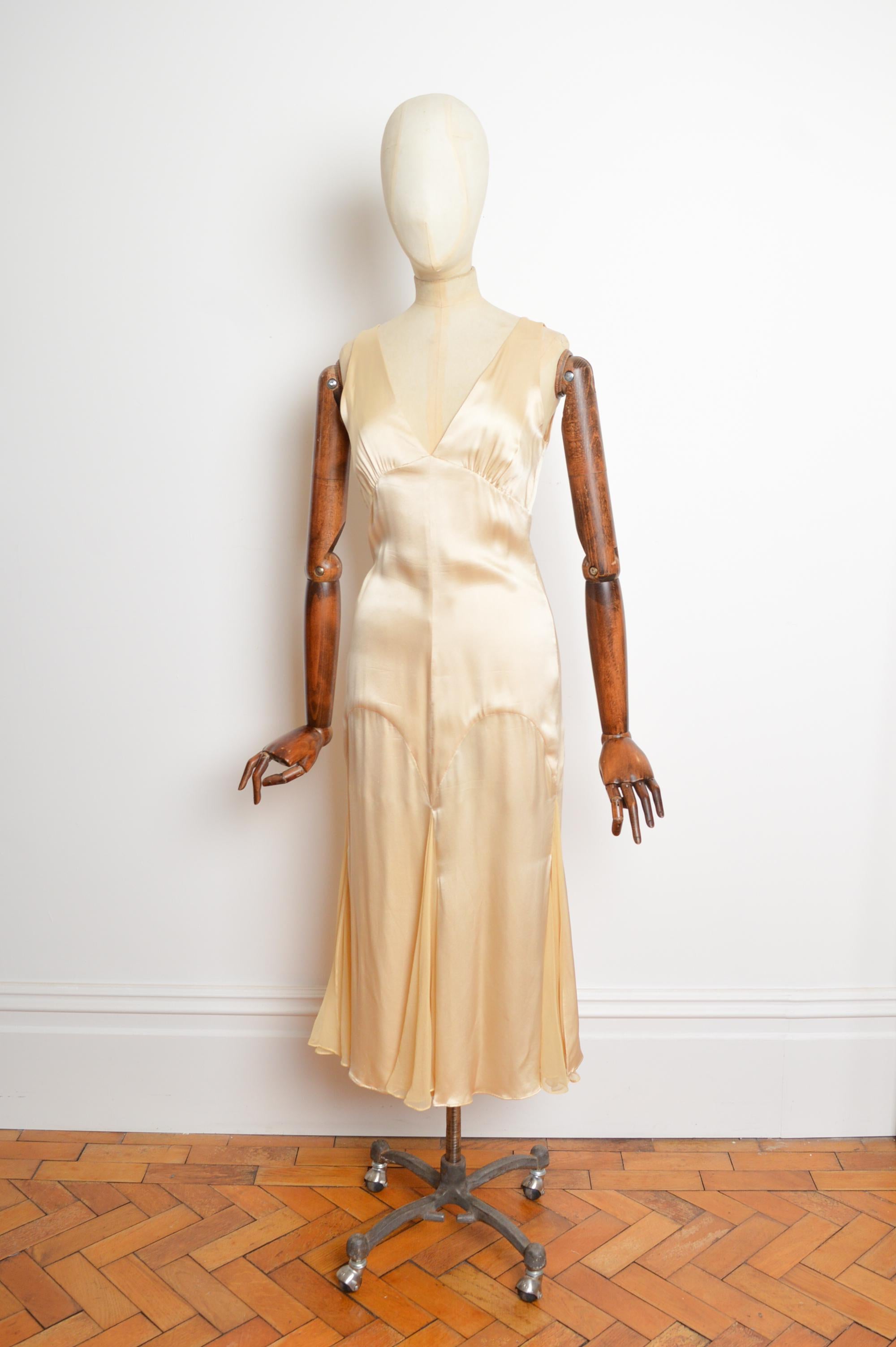 An Elegant 2000's Vintage Emanuel Ungaro Ensemble in Nude-Cream.
The set comprises a Satin slip dress and matching cropped Silk bolero jacket.
The Dress features a plunged neckline, key-hole slit back, fitted waist line and pleats across the bottom