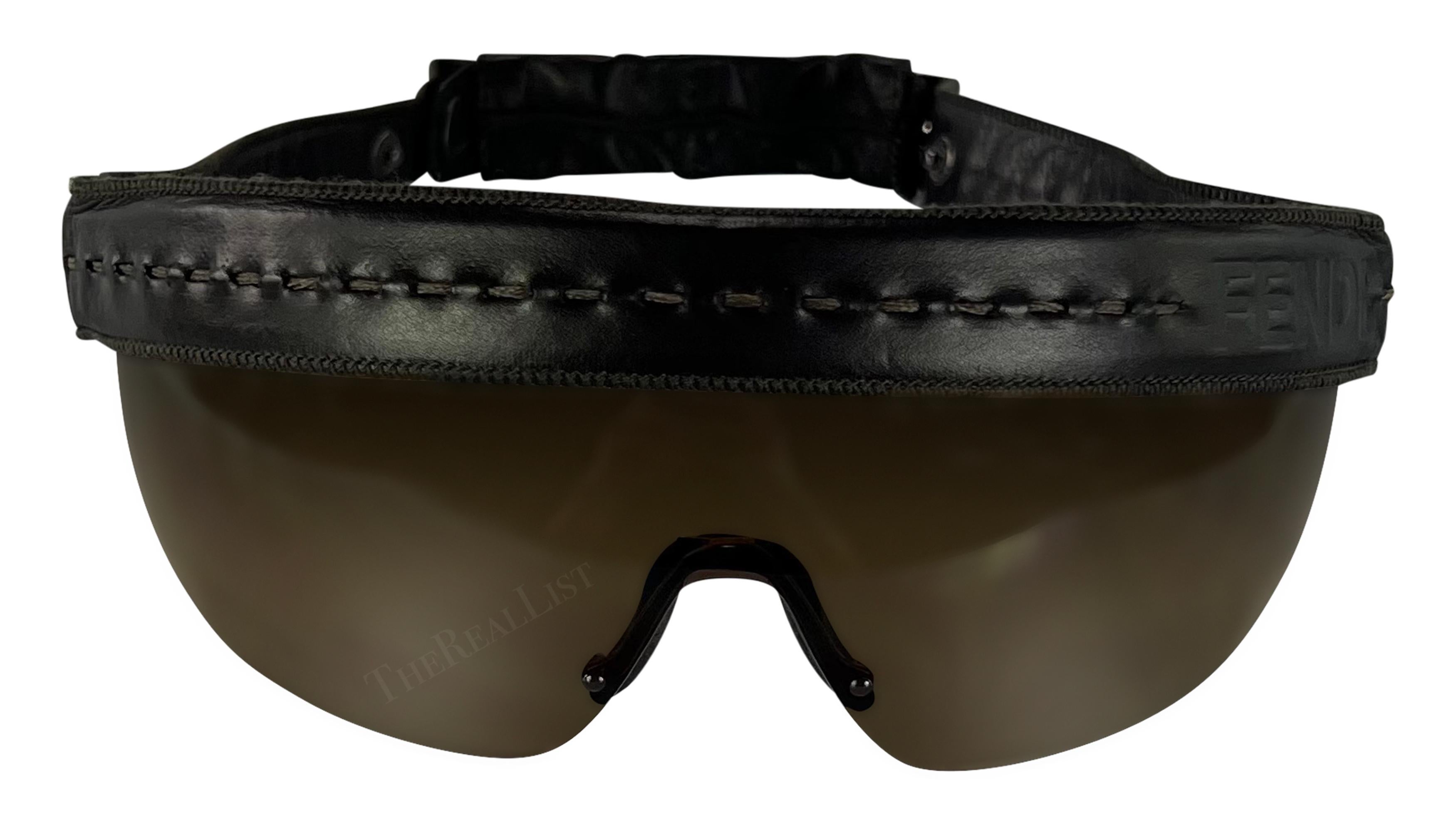 Elevate your style with these vintage brown Fendi shield sunglasses, designed by Karl Lagerfeld in the 2000s. These oversized shades feature a braided leather headband, complete with long leather fringe accents that cascade down the back. These