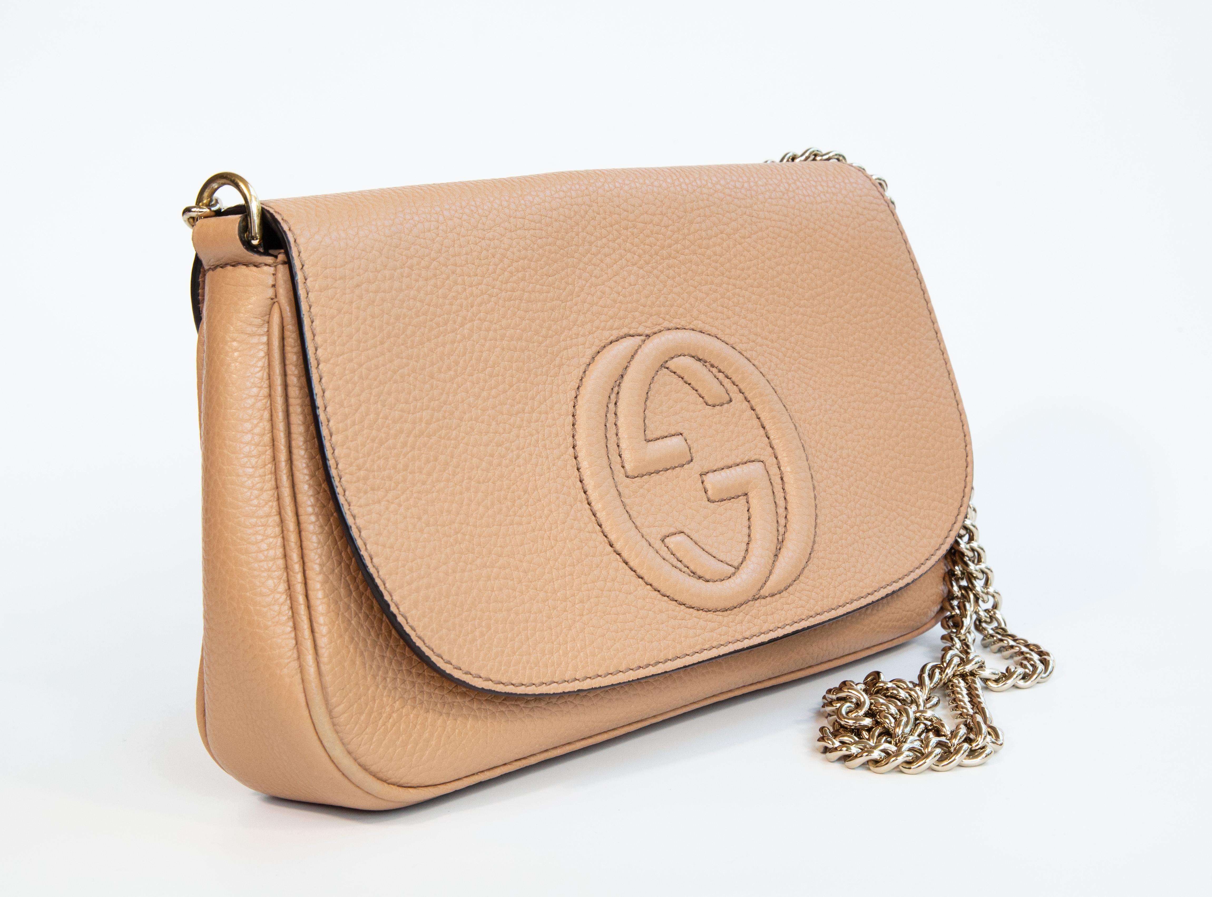 Sac à bandoulière à long rabat Gucci SOHO en cuir beige et ornements dorés clairs. L'intérieur est doublé de tissu beige et, à côté du compartiment principal, il comporte deux poches latérales dont l'une est dotée d'une fermeture à glissière. Le sac