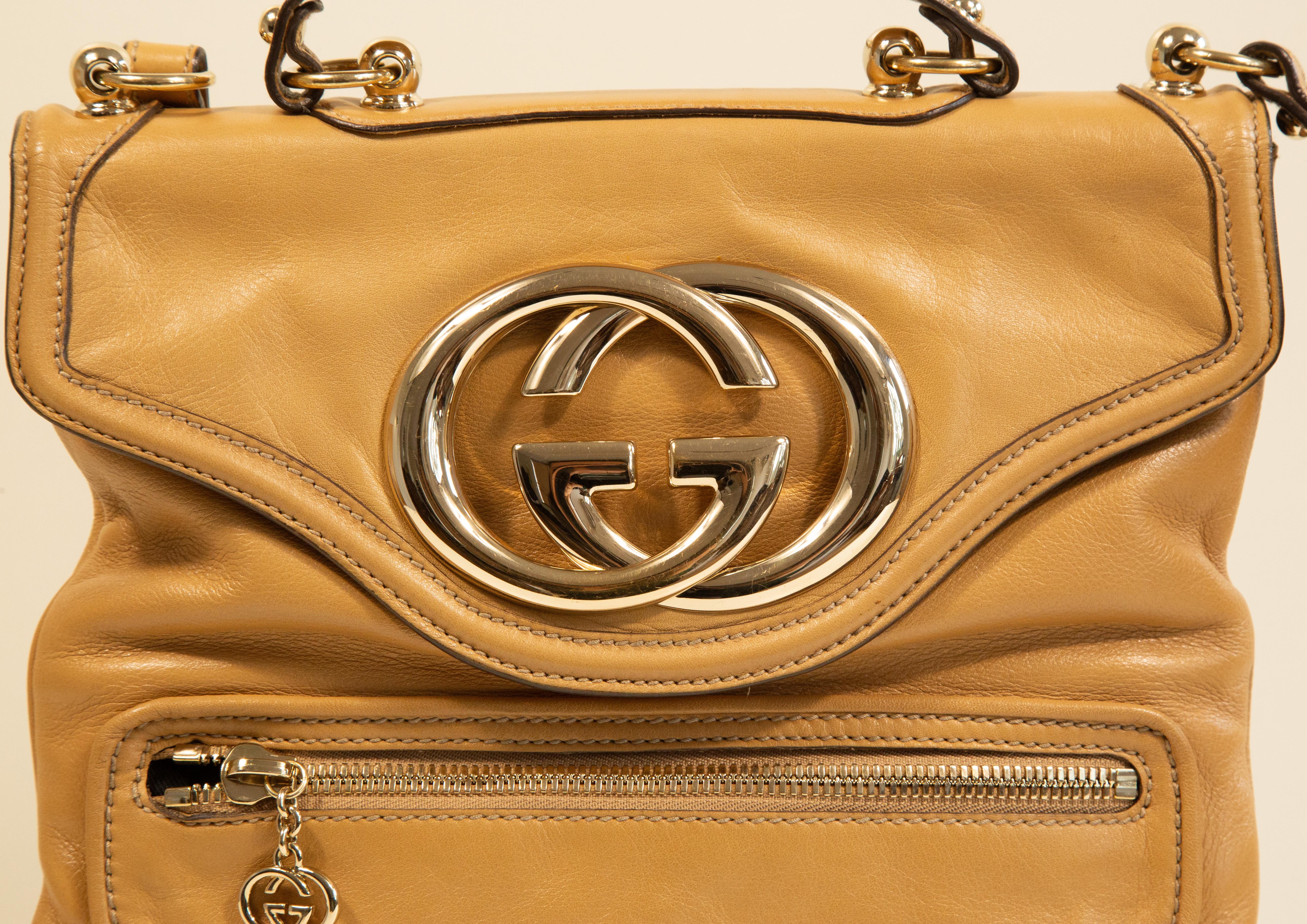 Sac à bandoulière/à poignée Gucci Britt avec grand logo GG en métal. La quincaillerie est dorée et le sac est en cuir beige. L'intérieur est doublé de tissu rayé et, à côté du compartiment principal, il comporte une poche latérale à fermeture