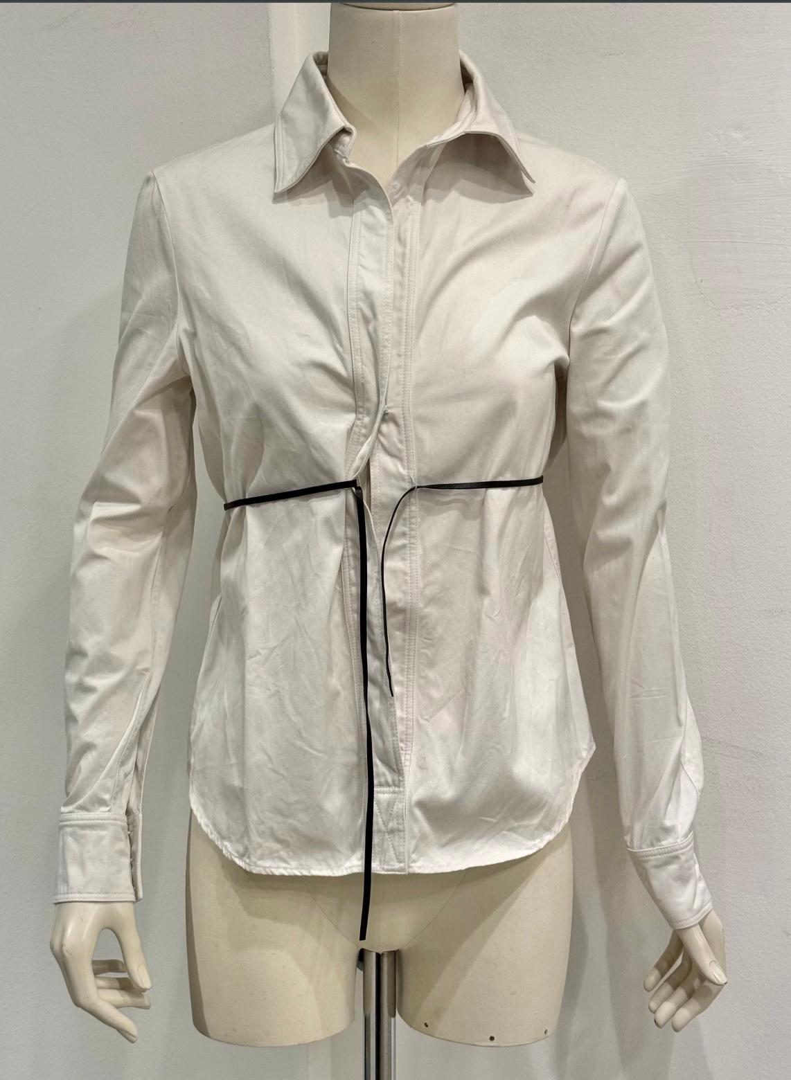 2000s Gucci by Tom Ford leather cord shirt

This Gucci shirt from the Tom Ford era in the 2000s is crafted from crisp white cotton with a sleek, tailored silhouette. The design is elevated by a contrasting black leather cord detail that cinches the