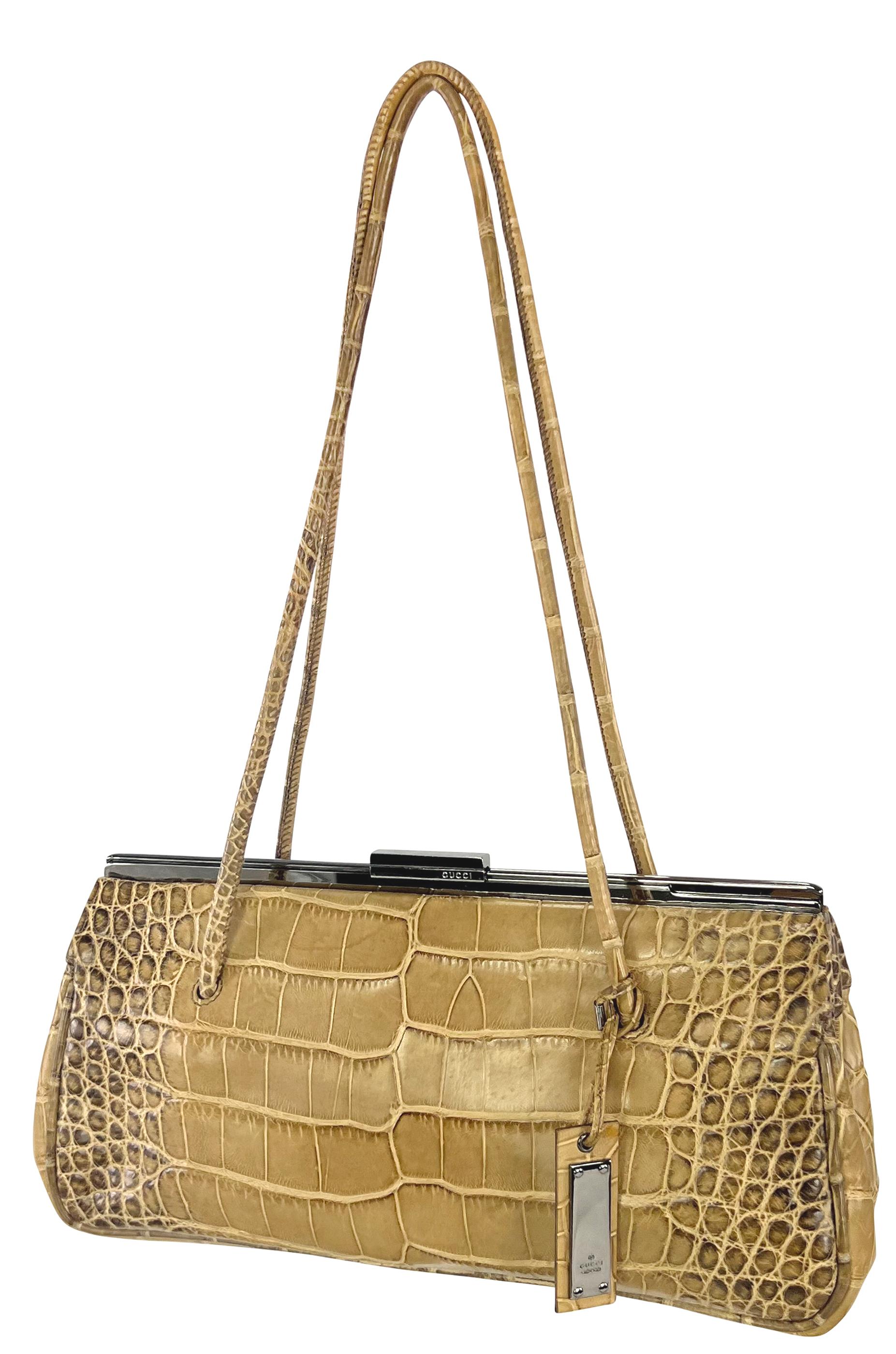 From Gucci’s early 2000s collection by Tom Ford, this structured shoulder bag is crafted from genuine tan crocodile skin. It features a sleek silhouette with a sliding lock closure, a rigid frame, and elongated shoulder straps, finished with a