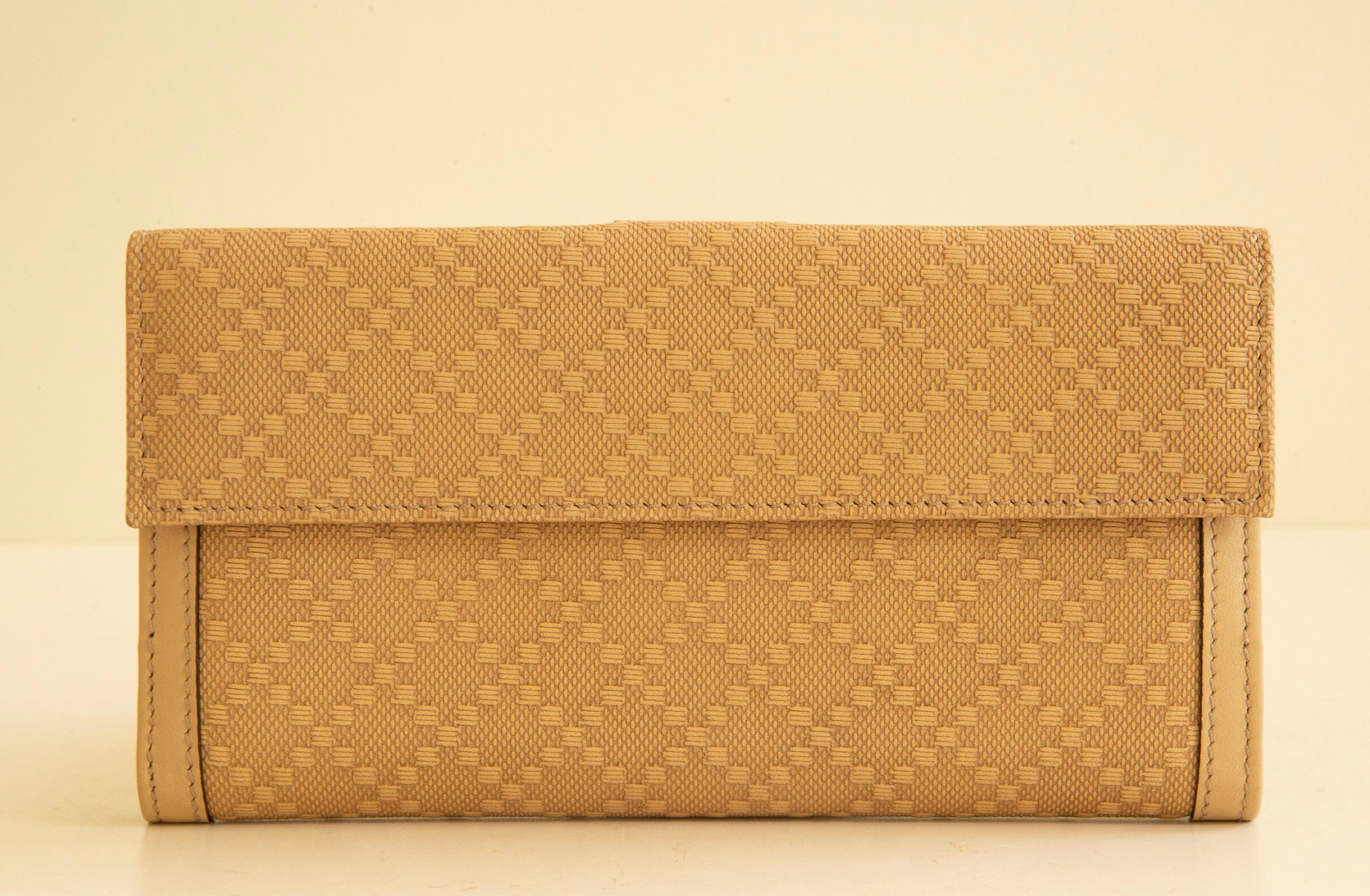 A Gucci continental wallet made of beige fabric with a diamante pattern, beige 
leather trim, and silver tone hardware. It features a separate compartment for coins,
and a compartment for banknotes and several slip pockets for cards. The wallet 
has