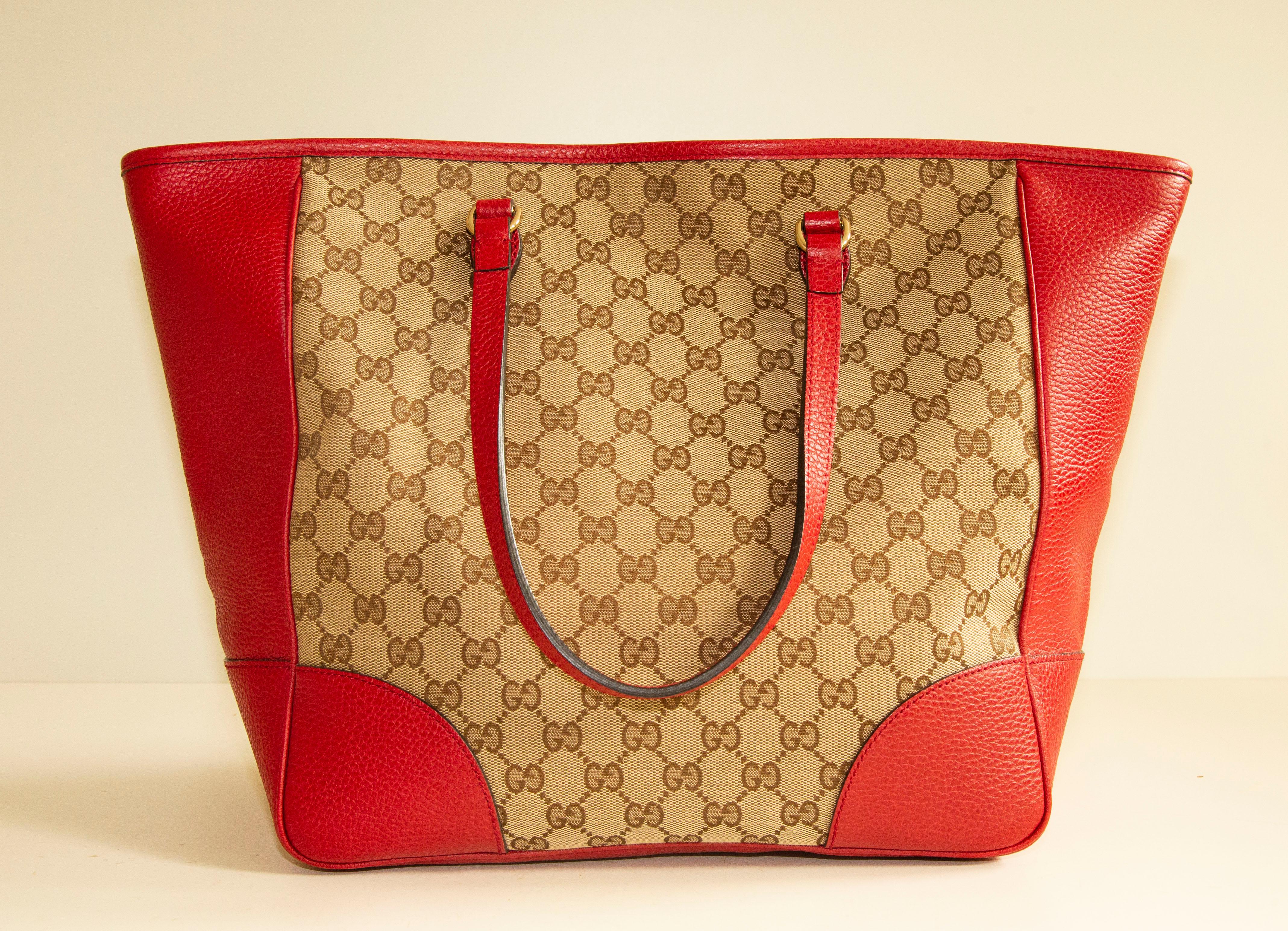 A large Gucci shoulder bag/top handle bag made of GG canvas with red leather trim and gold toned hardware. The interior is lined with canvas and next to the major compartment it features three side pockets of which one has a zipper. The condition is