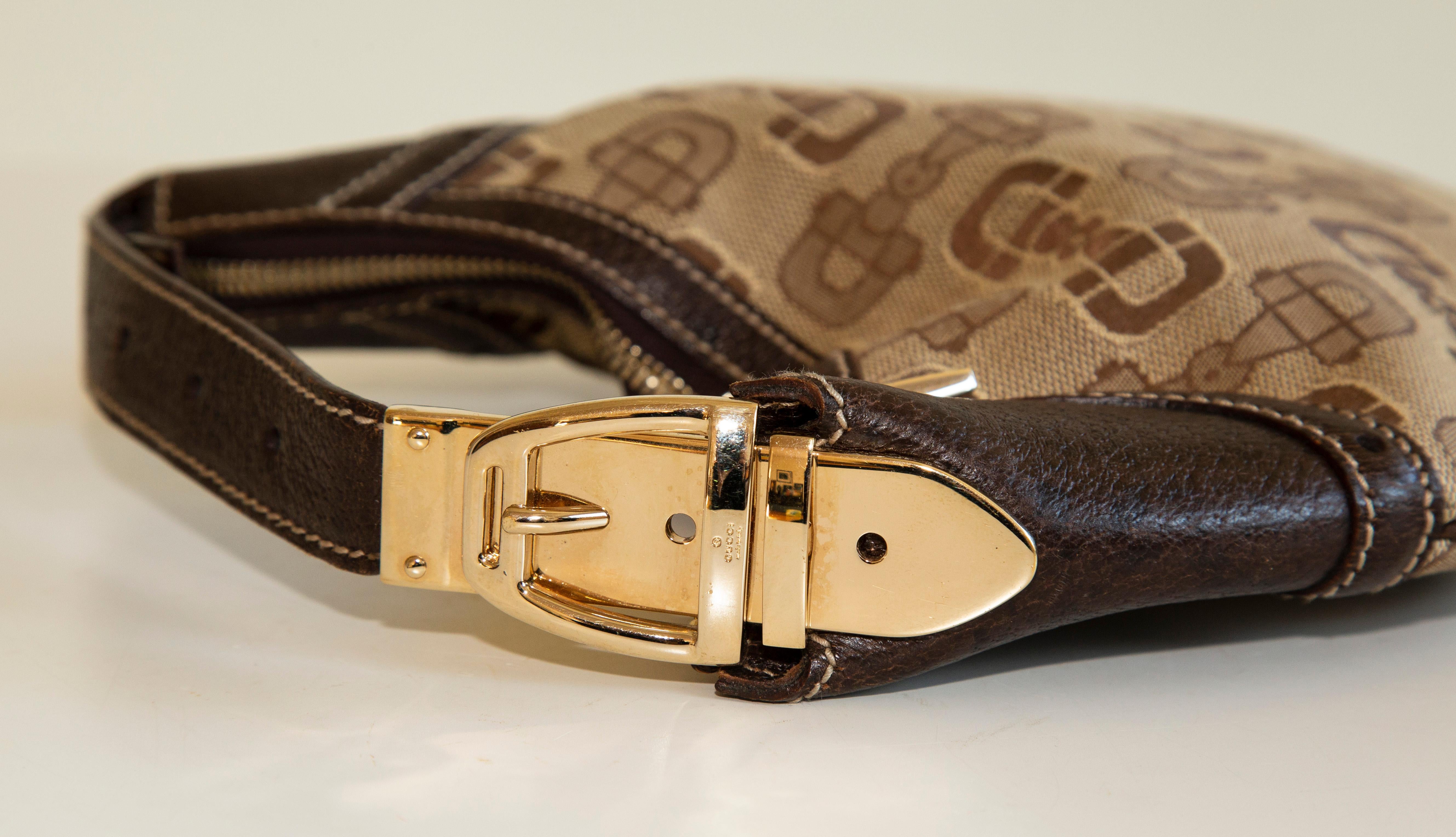 A mini Gucci hobo handbag. The bag is made of canvas with a horse bit patternand it features brown leather trim and gold tone hardware. The interior is lined with brown fabric and next to the main compartment it has a side pocket with a zipper. The