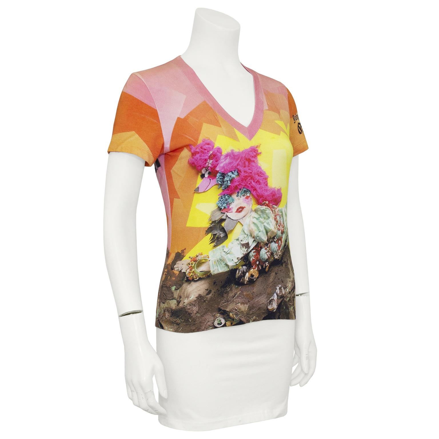 Fun and vibrant John Galliano graphic, cotton, v neck, short sleeve t-shirt from the early 2000s. The orange, pink and yellow abstract background features a quirky doll with a bright pink poodle wig, fun makeup and a seashell embellished outfit.