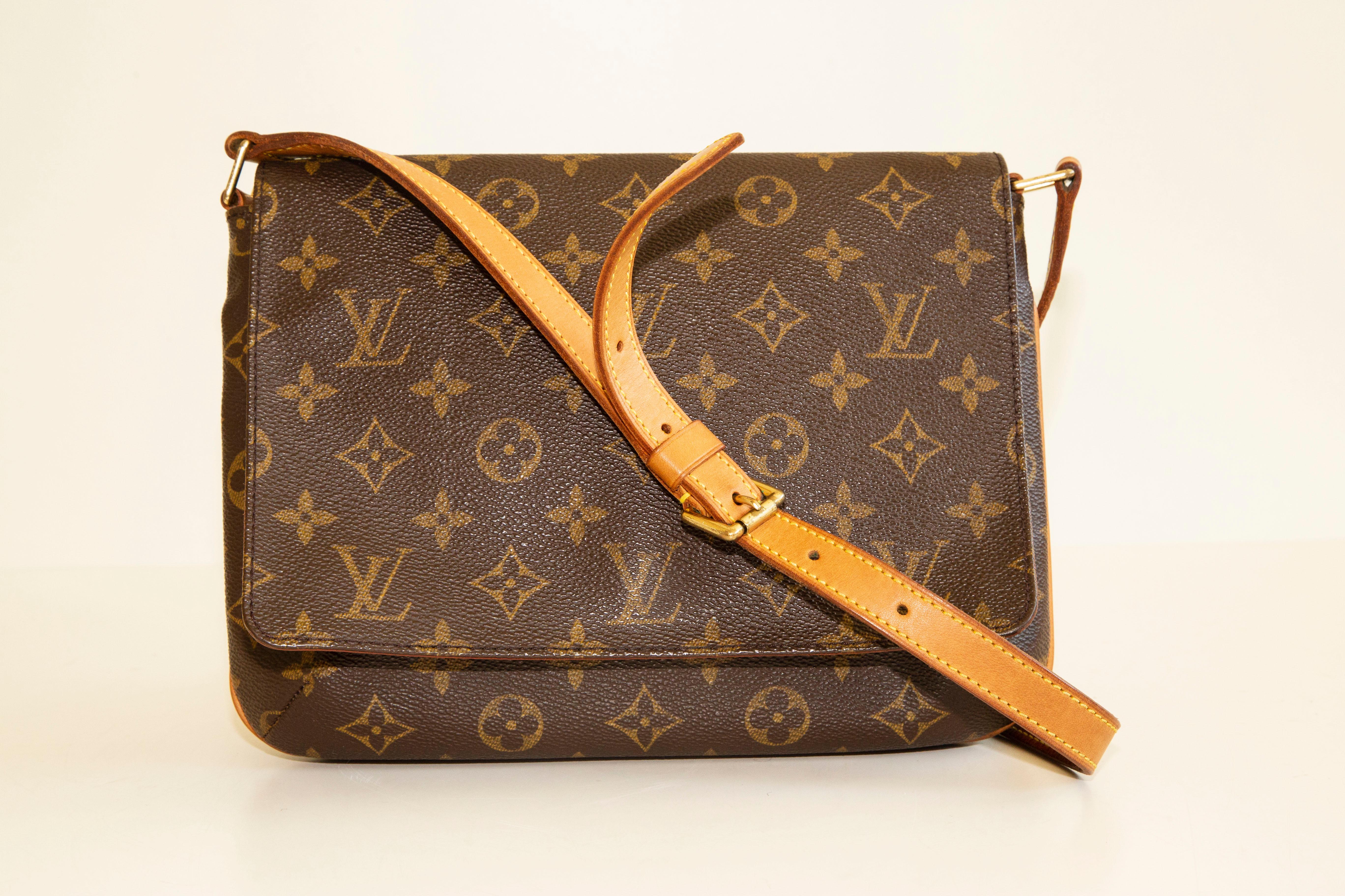 An authentic vintage Louis Vuitton Musette Tango shoulder bag. The bag features a Louis Vuitton monogram canvas and a tan leather strap. The interior is lined with orange suede like fabric, and next to the major compartment, there is one slip