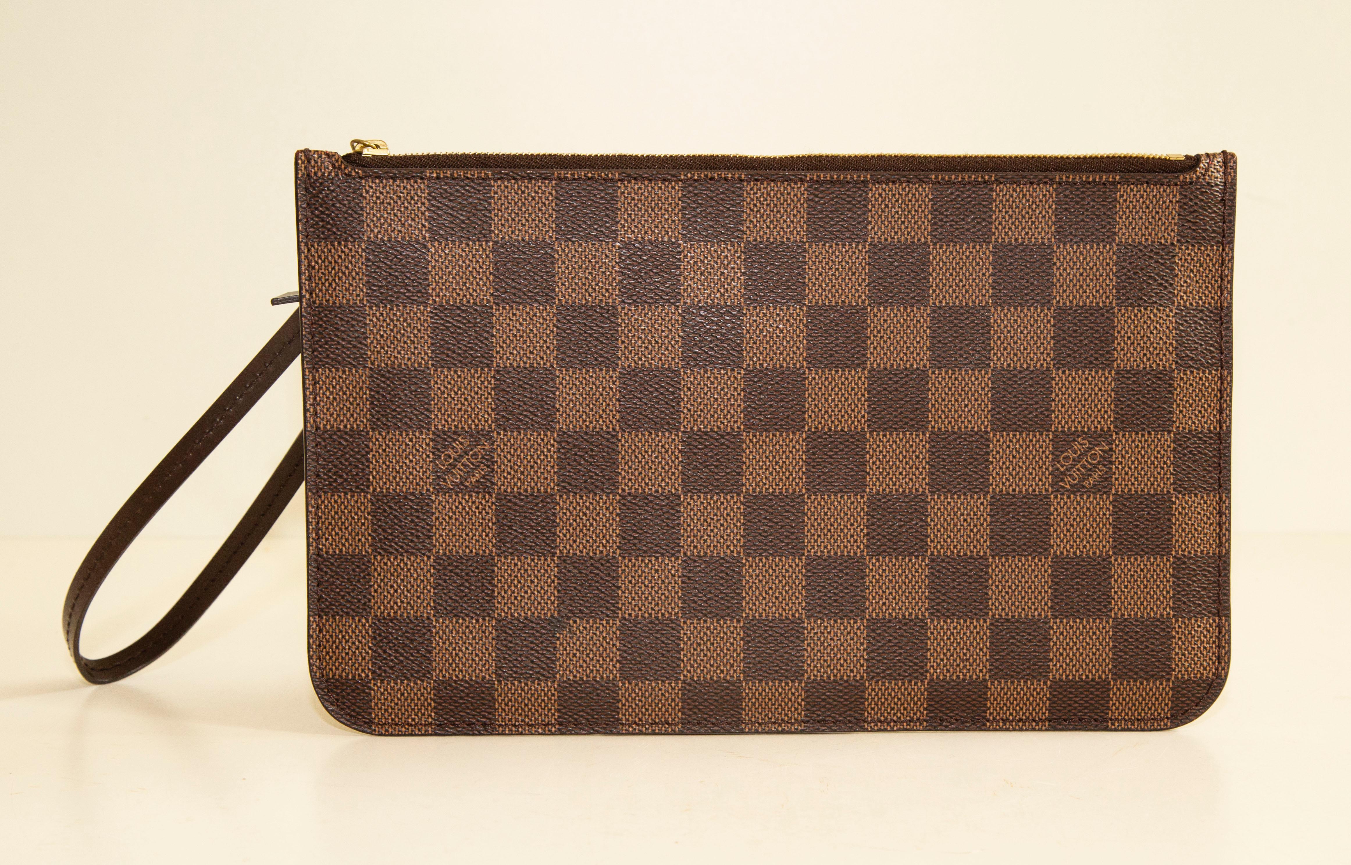 Pochette Louis Vuitton en toile enduite Damier Ebene, garnie de cuir marron foncé et de ferrures dorées. Peu utilisé et en très bon état. 

Mesures
Largeur : 24,5 cm
Hauteur : 15 cm