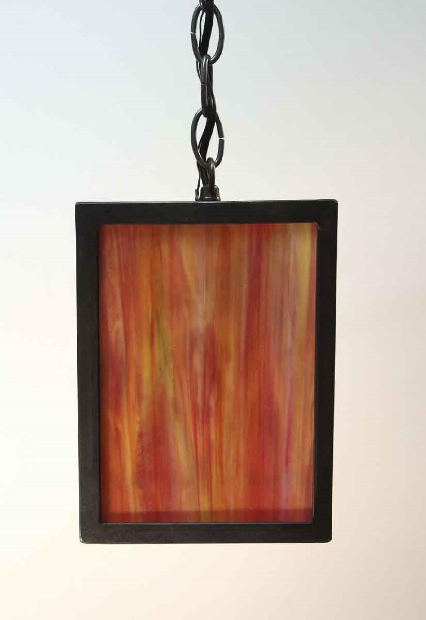 Simple handcrafted Mid-Century Modern or Prairie style 2000s iron framed lantern with red, orange, brown and yellow stained glass and a brass chain. This can be seen at our 400 Gilligan St location in Scranton. PA.