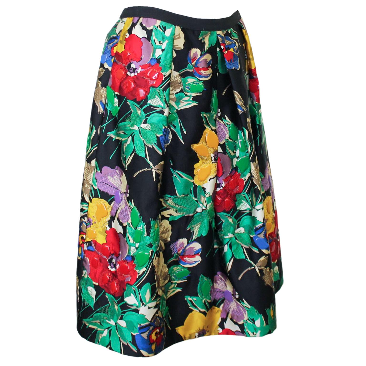 Early 2000s Oscar de la Renta black silk skirt with a vibrantly colored floral print. The skirt has an inverted center pleat and mirrored single pleats on either hip. Same in the back. Zips up the back and has a black grosgrain waistband. The floral