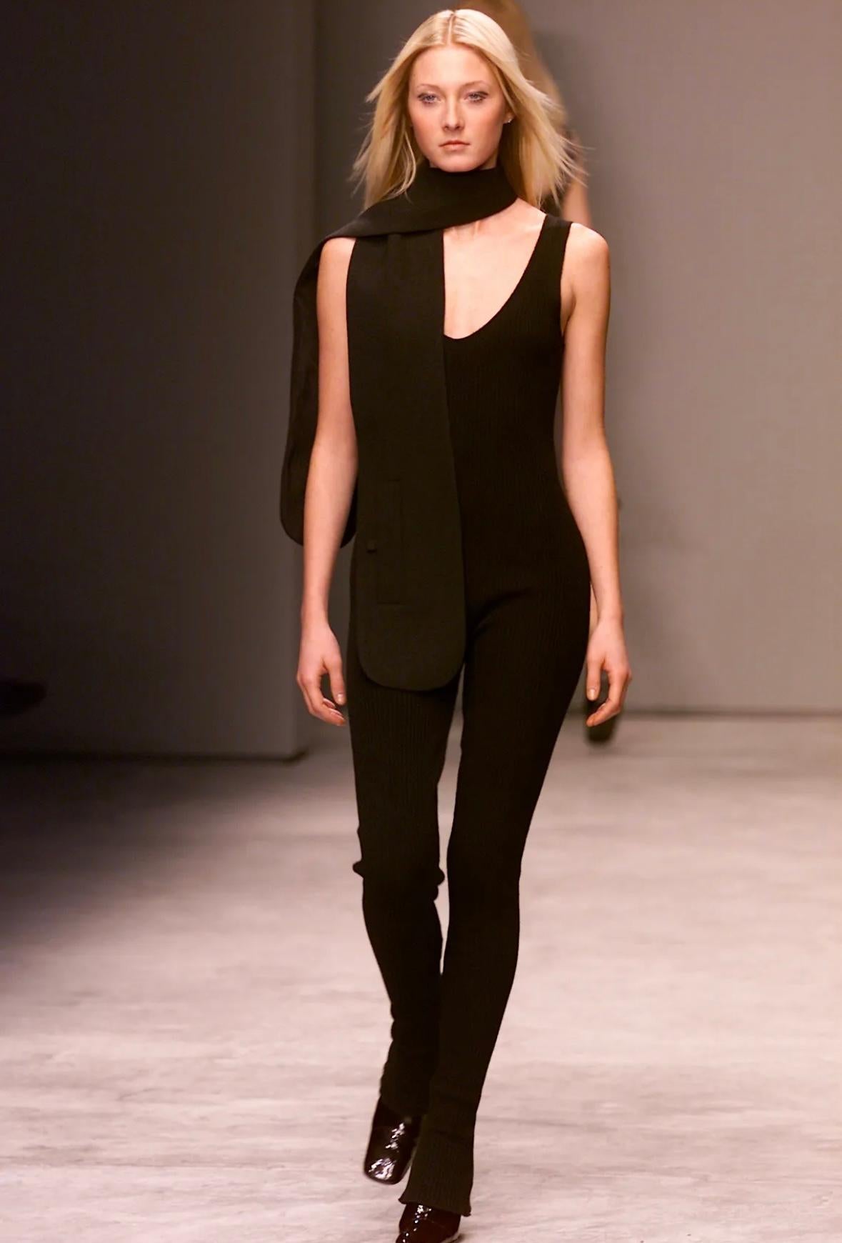 Voici un fabuleux body Prada en maille noire, dessiné par Miuccia Prada. Issu de la collection Automne/Hiver 2001, ce fabuleux catsuit est entièrement tricoté en côtes et présente un large décolleté, de larges bretelles de type tank et des poignets