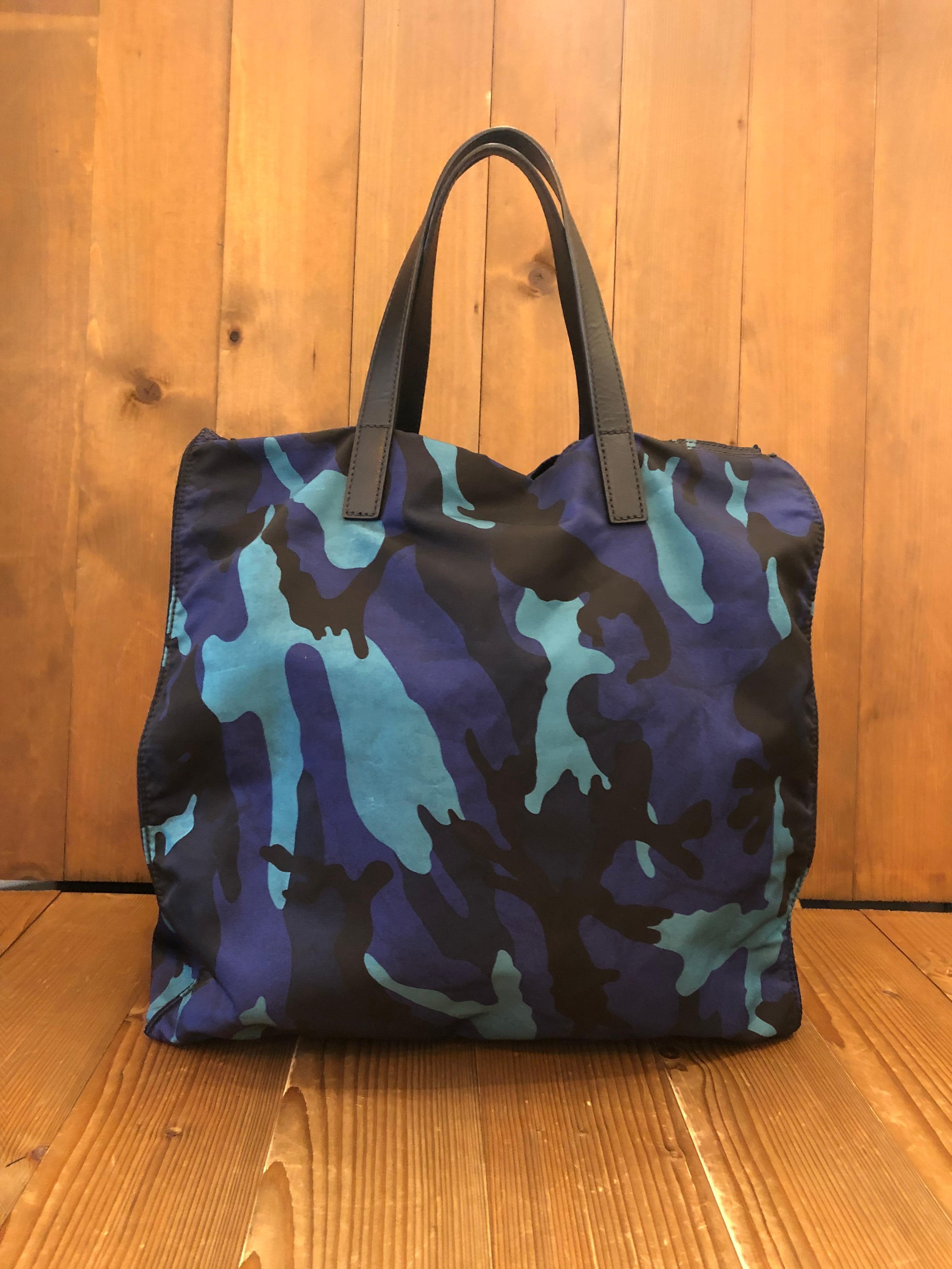 Ce sac fourre-tout à double sens de PRADA est confectionné en polyester camouflage marine/bleu et en cuir Saffiano. Ce sac fourre-tout léger présente des accessoires noirs mats, des poignées en cuir Saffiano et une bandoulière amovible qui permet de