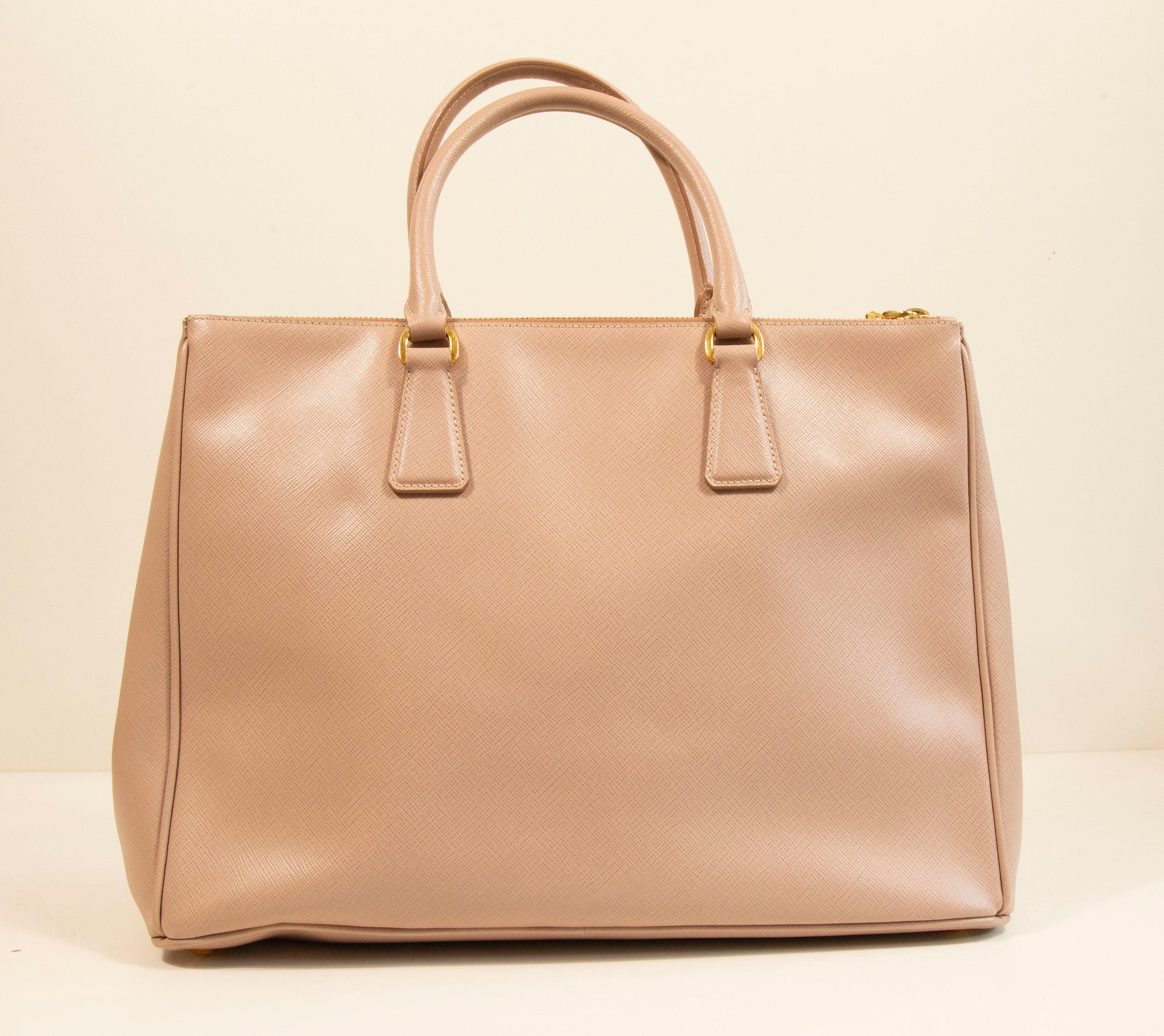 Prada Galleria handbag made of saffiano leather in light pink/nude with gold toned hardware. The interior is lined with Prada logo synthetic fabric, and next to the major compartment it features three side pockets of which one has a zipper. In