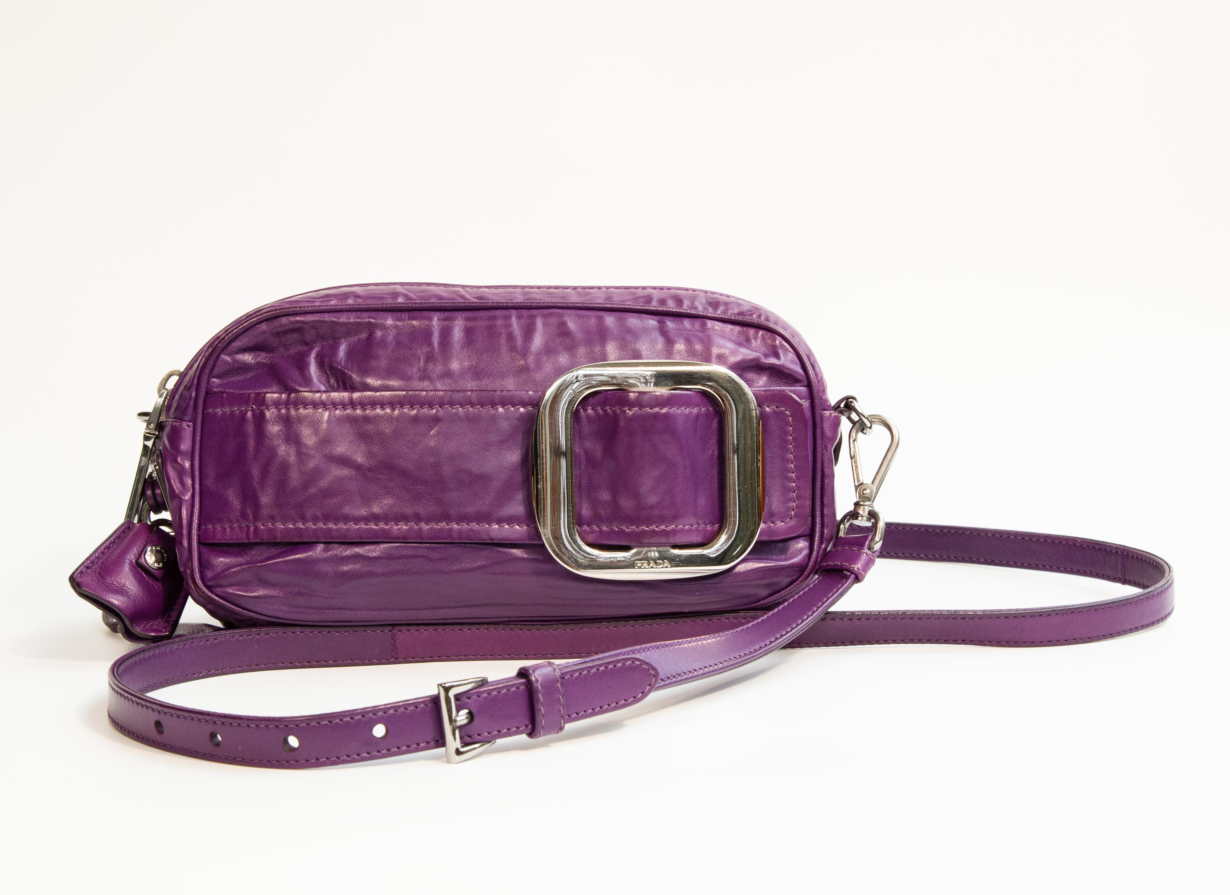 Una borsa di Prada in pelle increspata viola con finiture in argento. L'interno è foderato in morbida pelle beige e, accanto allo scomparto principale, presenta due tasche laterali di cui una con cerniera. La borsa può essere indossata come una