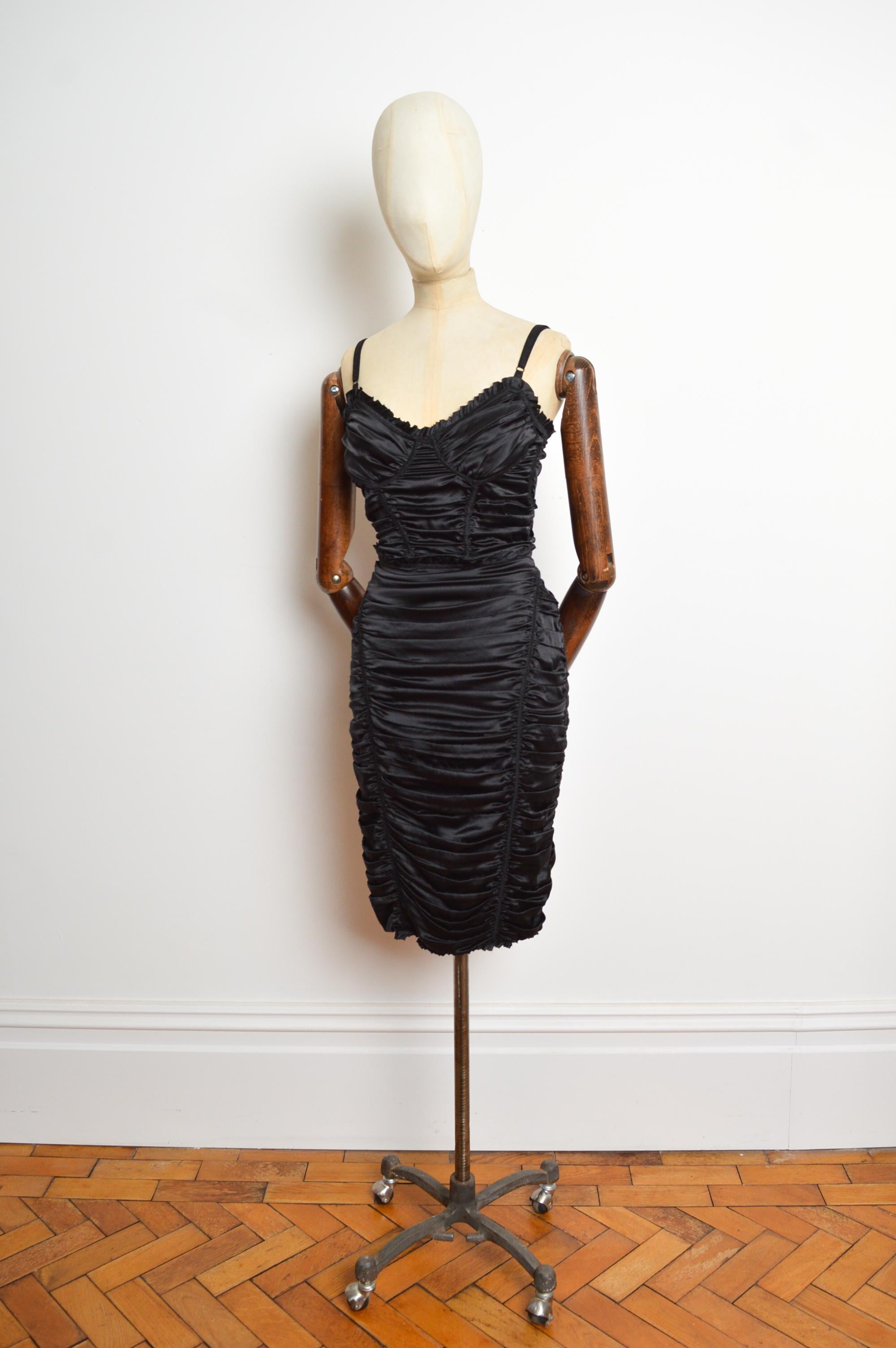 Un vestido atemporal de la firma Dolce & Gabbana de los años 2000. Confeccionada en seda satinada negra, con una silueta ceñida. Tirantes totalmente ajustables y cremallera expuesta en el reverso. 
Talla; recomendada U.K. 8
Las medidas se indican en