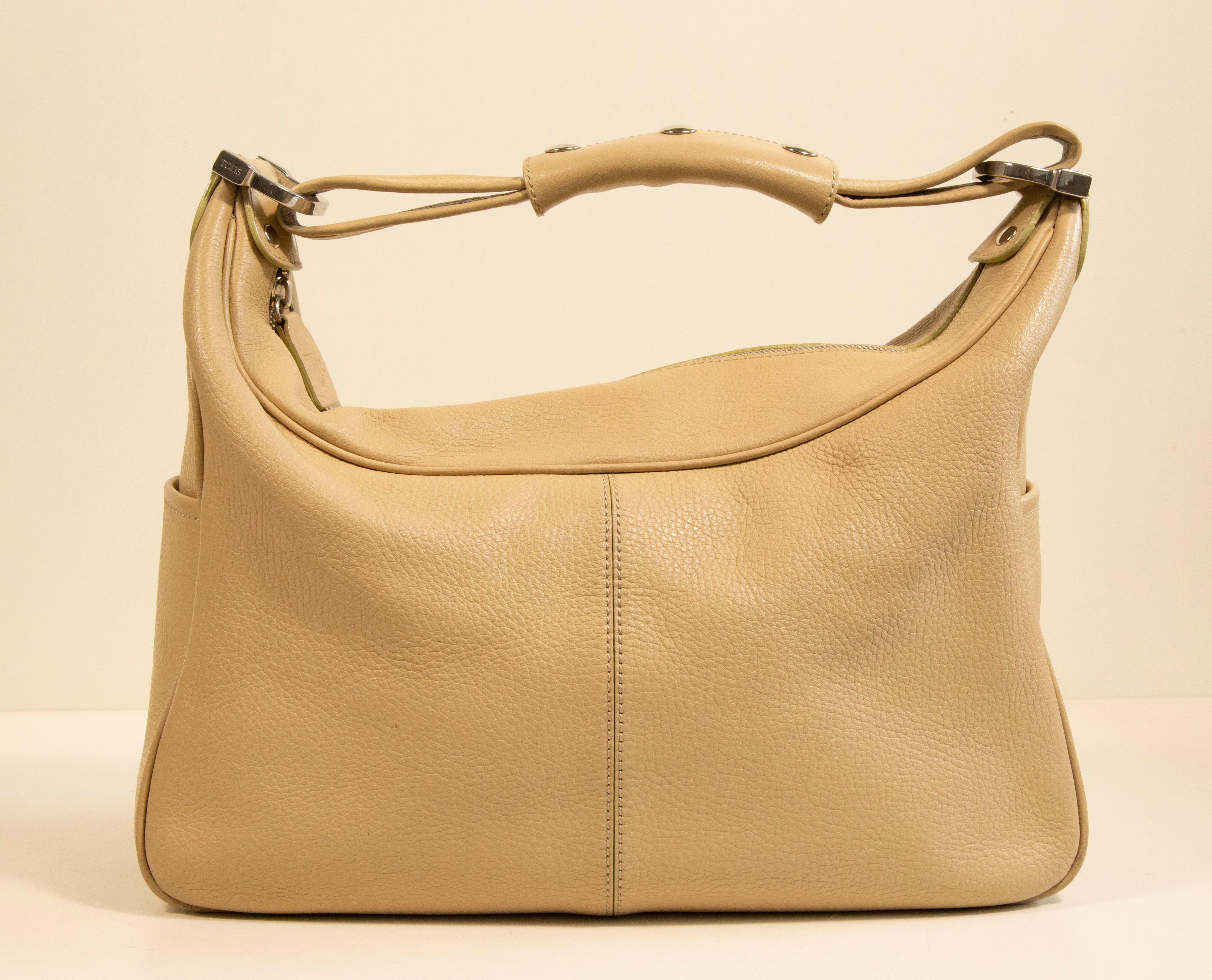 Tod's shoulder bag made of beige leather with silver toned hardware. The interior is lined with brown fabric and next to the major compartment it features one zipped pocket. In addition , there are two slide pockets on both sides of the bag. The bag