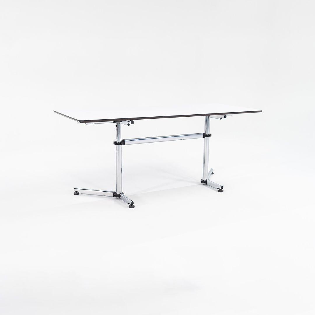 This is rectangular Kitos Table, designed by Swiss manufacturer USM Haller in 1990. This piece dates to the early to mid 2000s. The design includes a steel columnar base, and has steel support tubes under the top with a white laminate tabletop. The