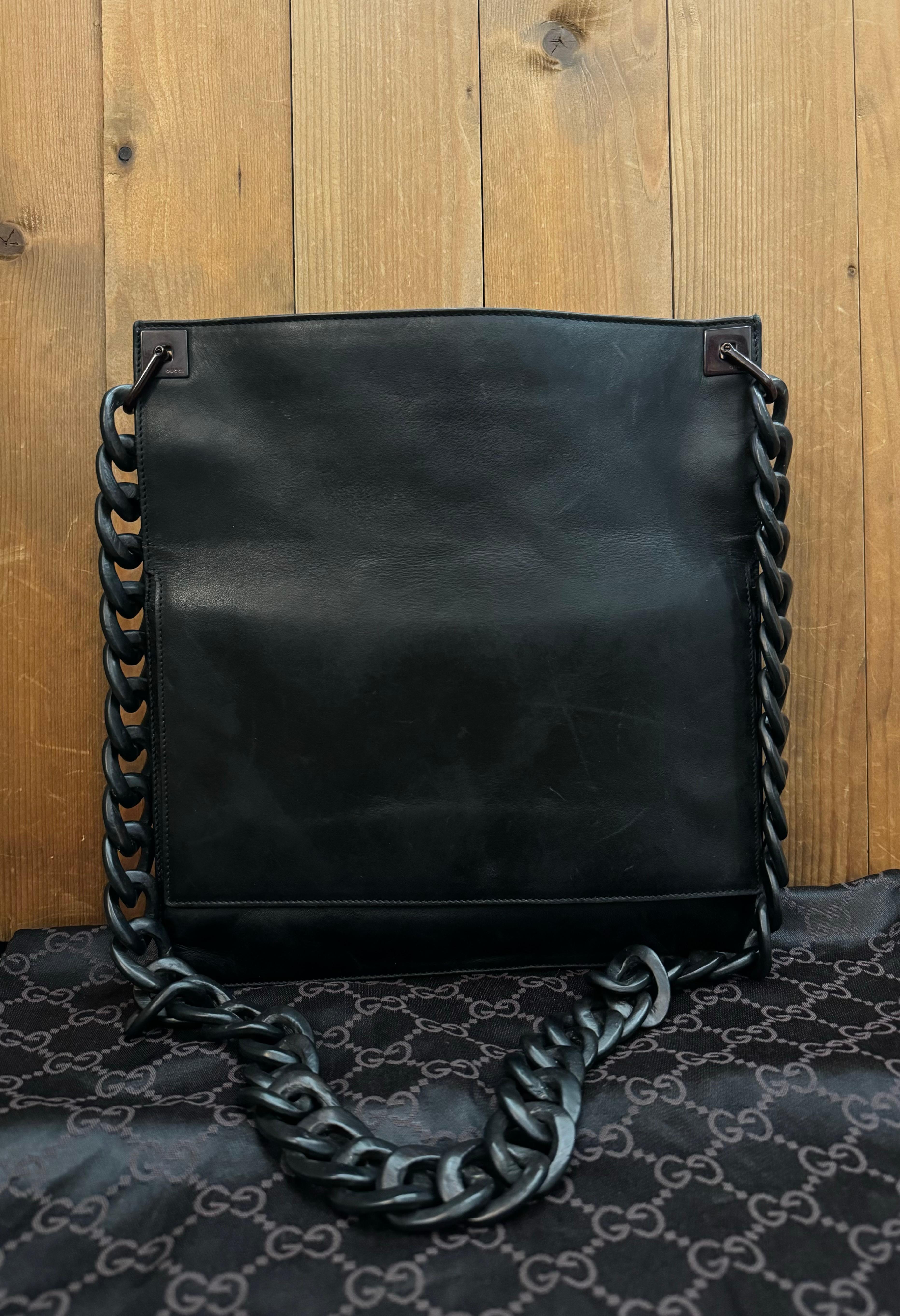 Diese flache Vintage-Messenger-Tasche von Gucci ist aus schwarzem, glattem Kalbsleder gefertigt und mit einer Holzkette versehen. Der Deckel öffnet sich zum Hauptfach, das mit Veloursleder gefüttert ist und eine aufgesetzte Tasche enthält. Auf der