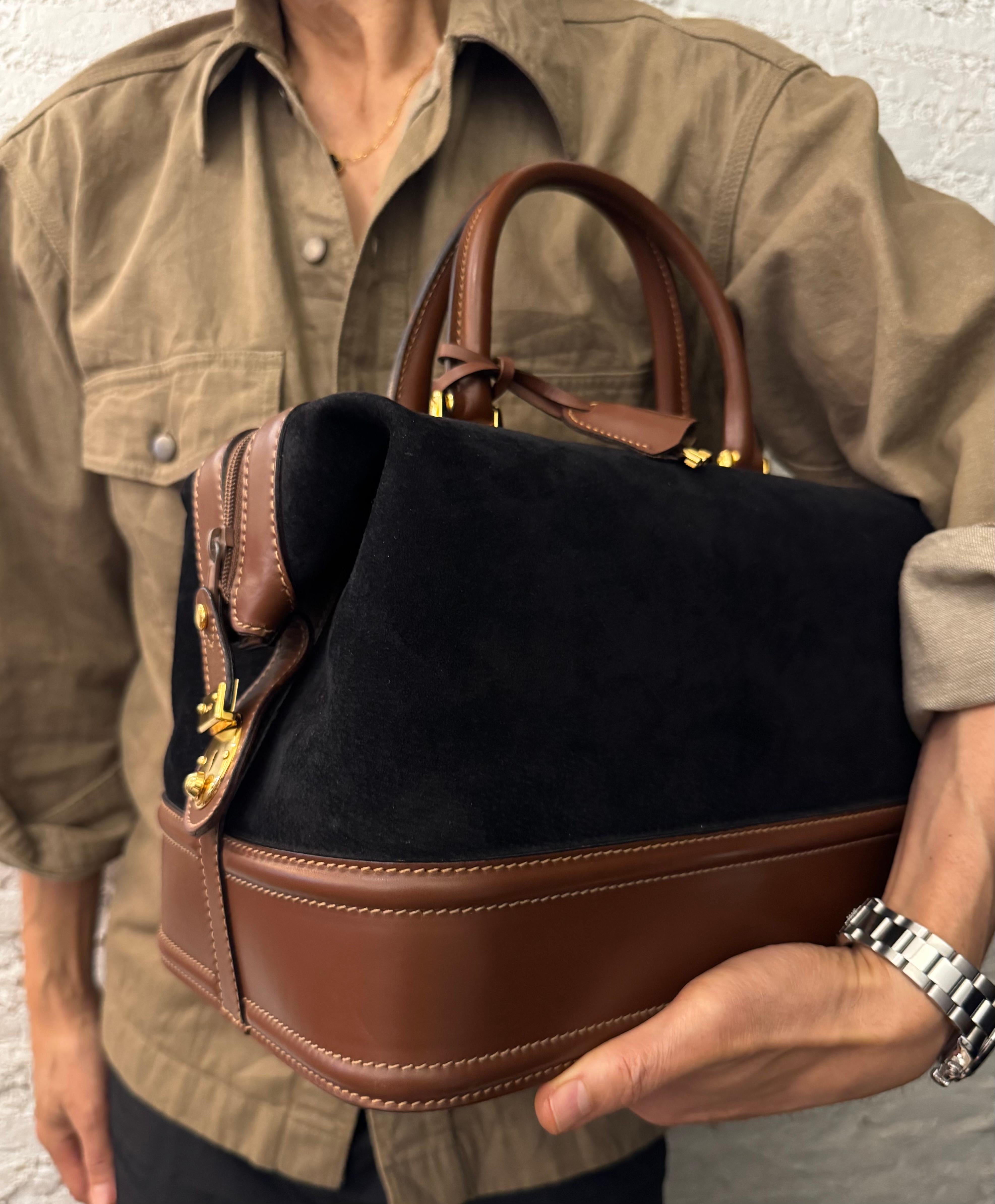 This rare vintage GUCCI vanity case is crafted of nubuck leather in black trimmed with smooth calfskin leather in brown featuring rolled leather handles. Top zipper closure opens to a brown suede interior with a zippered pocket and leather strap to