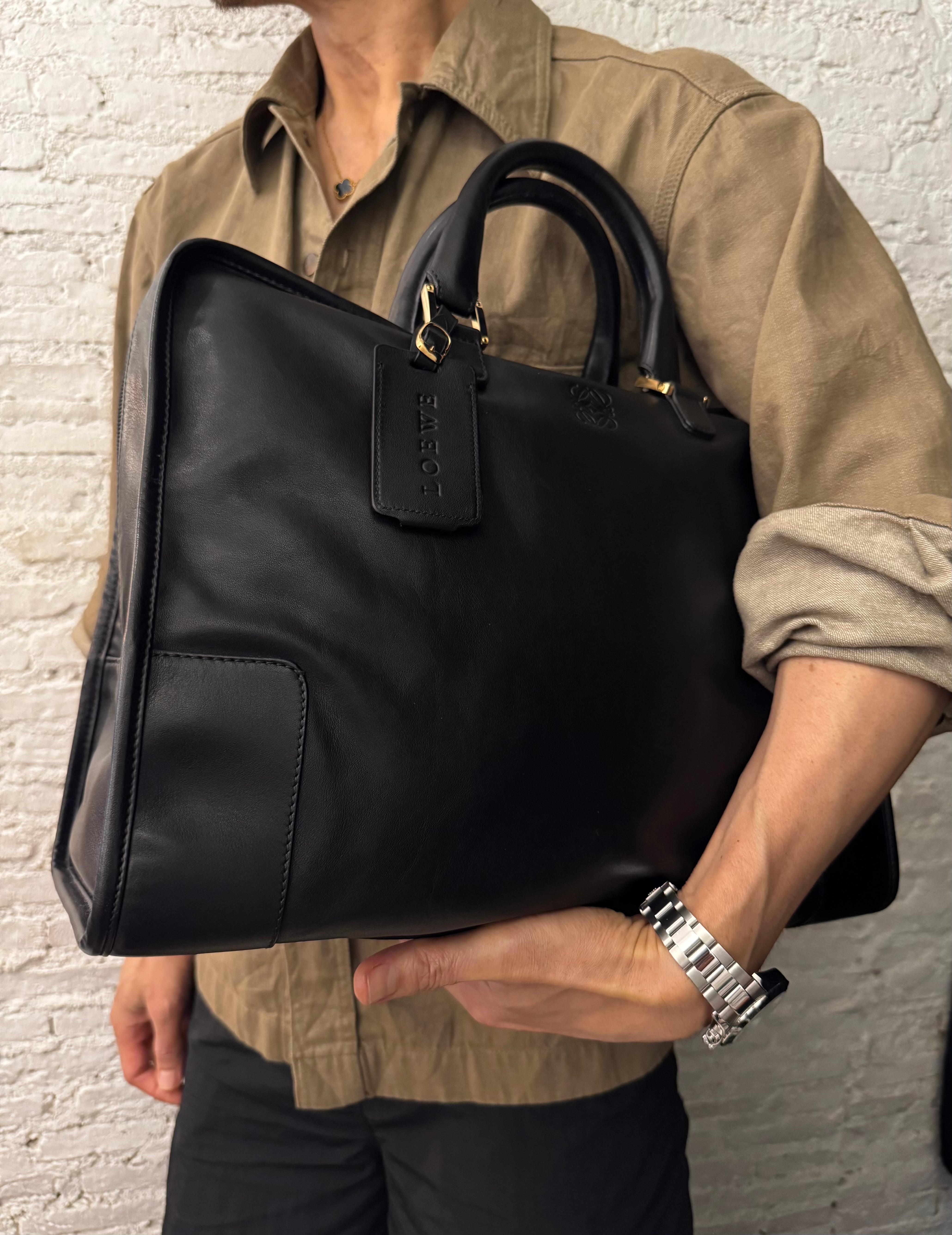 This vintage LOEWE Anagram boston bag is crafted of small gained calfskin leather in black featuring gold toned hardware. Top zipper closure opens to an anagramed fabric interior with a wide bottom featuring a zippered pocket. Made in Spain.