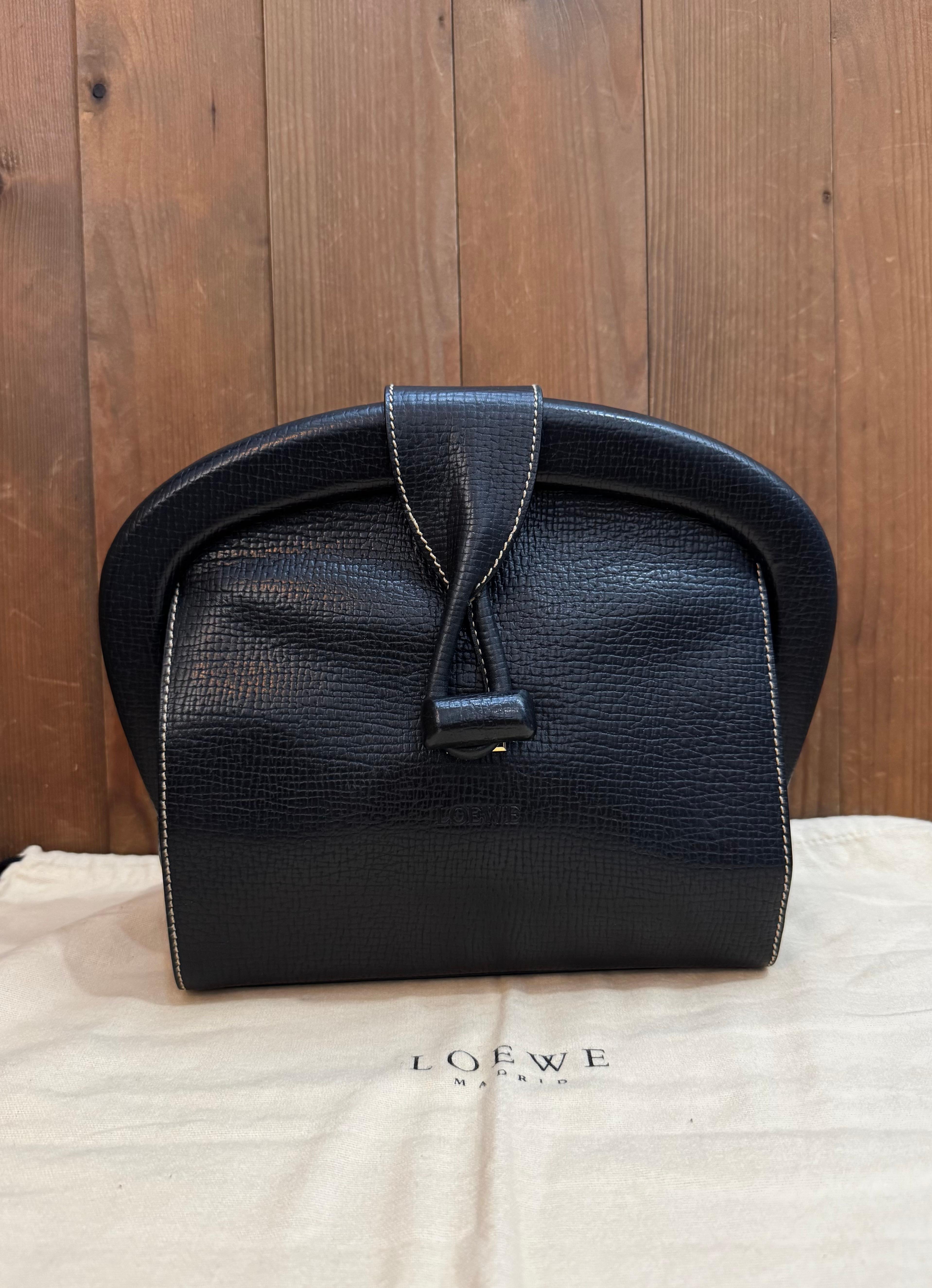 Questa pochette vintage di Loewe è realizzata in pelle bovina goffrata di colore nero. La chiusura frontale con serratura si apre su un interno in pelle beige con una tasca con cerniera. Prodotto in Italia. Misura circa 9 x 9 x 3,25 pollici. Viene