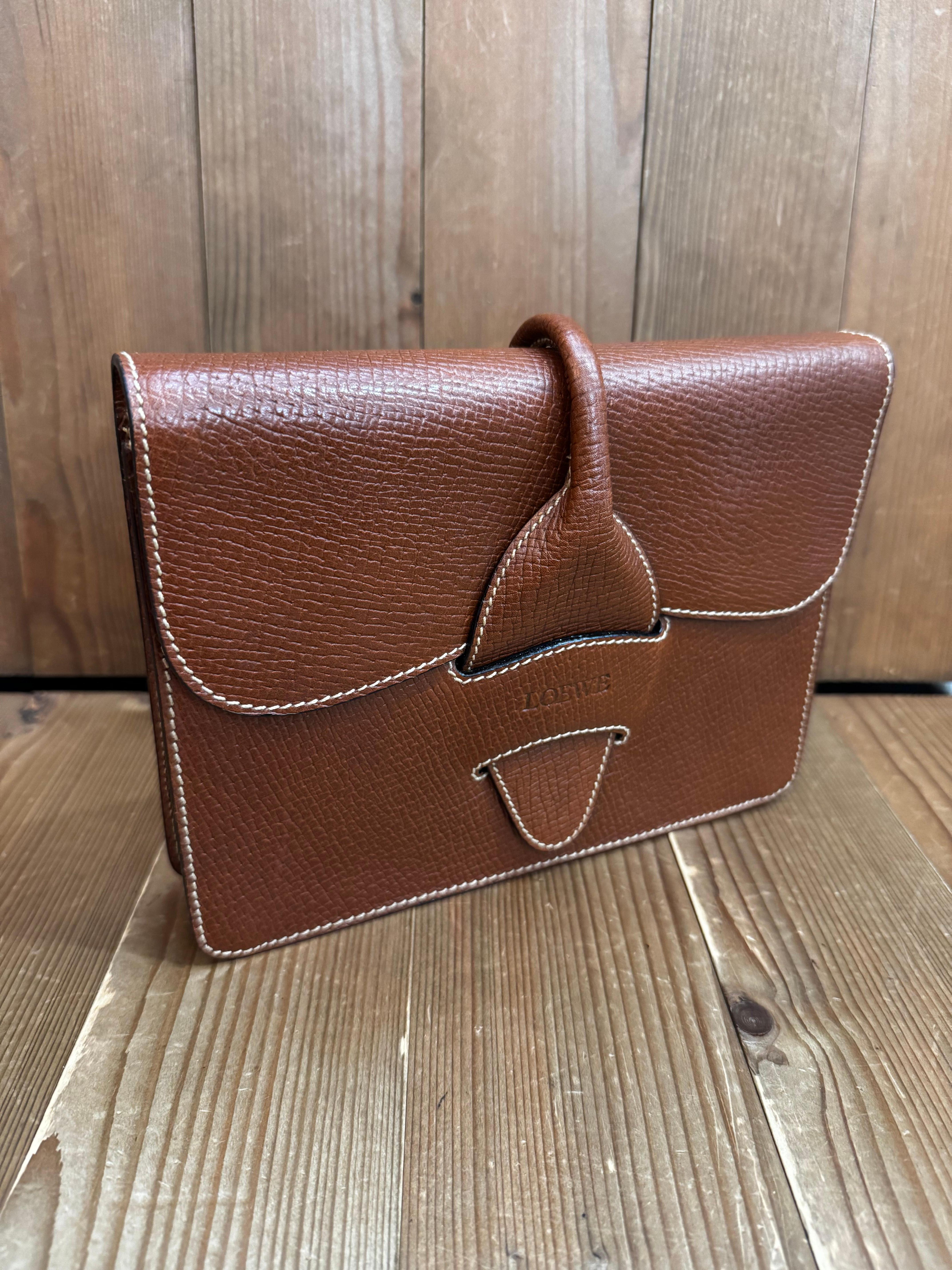 This vintage LOEWE box clutch is crafted of embossed cowhide leather in brown. Front flap closure opens to a beige leather interior featuring a zippered pocket. Made in Italy. Measures approximately 9.5 x 7 x 1.75 inches. Comes with dust