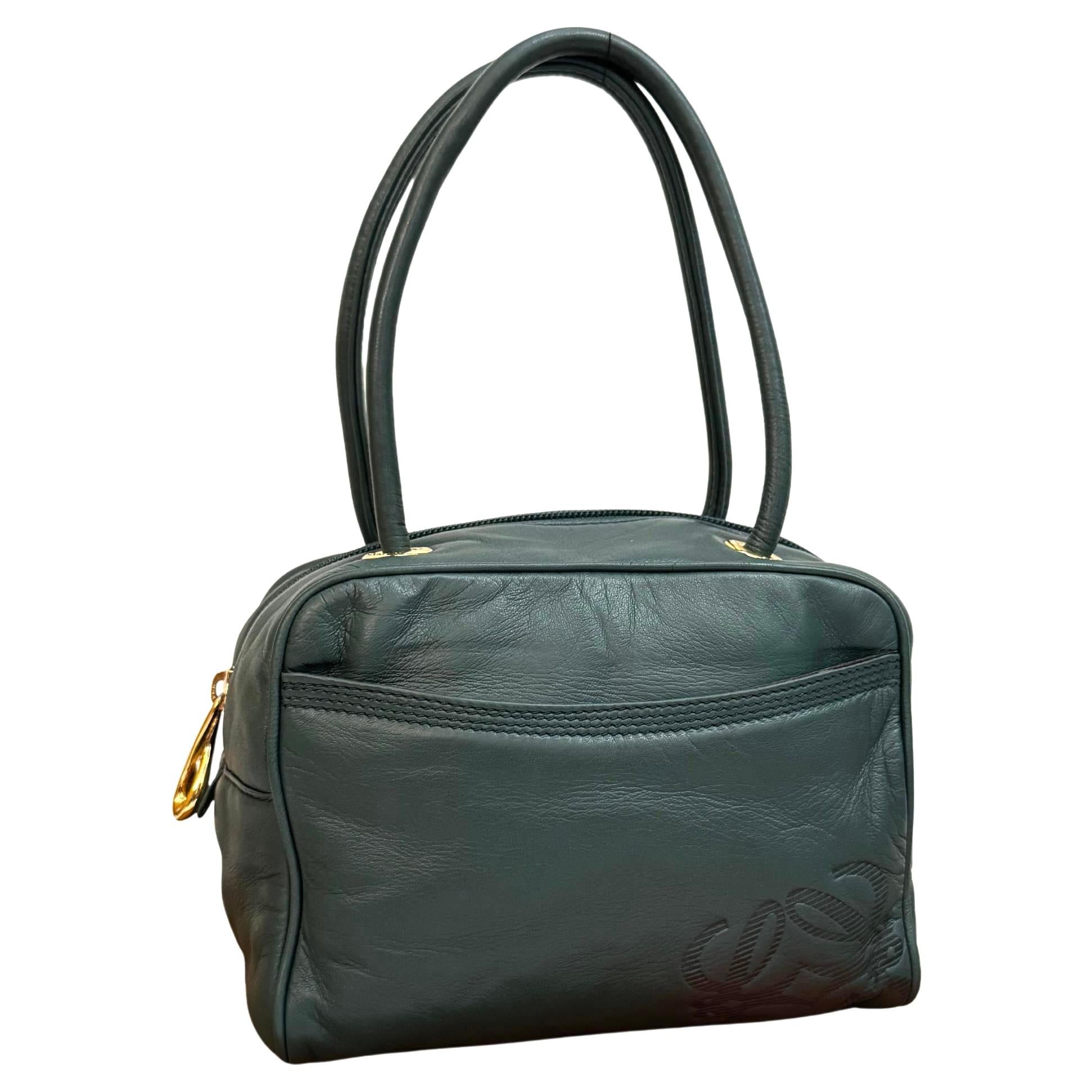 Este exquisito bolso de mano vintage LOEWE Anagram mini está confeccionado en piel de becerro fina y suave de color verde oscuro y herrajes dorados con asas de piel enrolladas. El cierre de cremallera superior se abre a un interior en jacquard