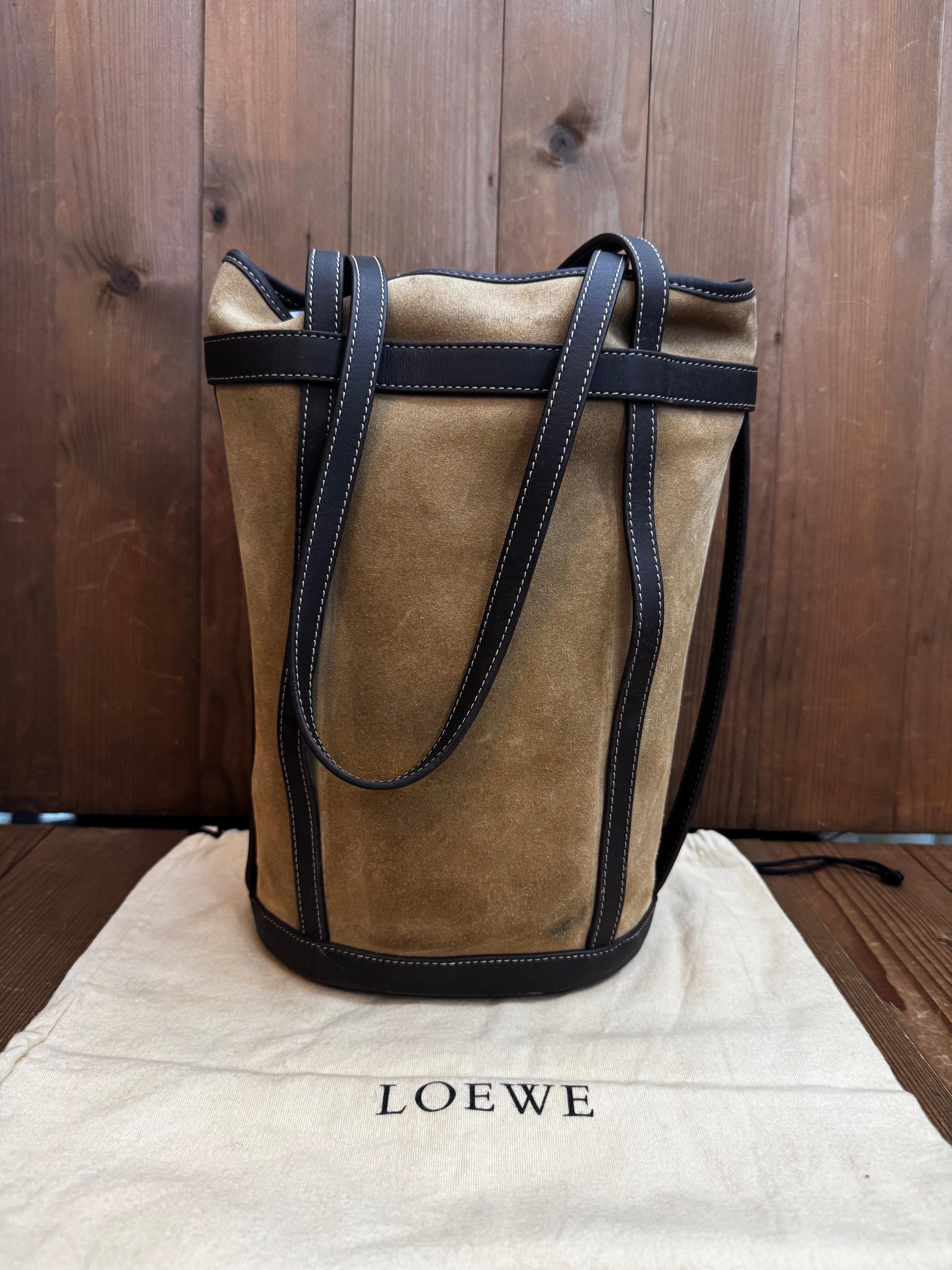 This vintage LOEWE Anagram bucket bag is crafted of calfskin suede in beige trimmed with smooth leather in dark brown featuring gold toned long shoulder straps of the same leather. Wide top opens to a spacious interior of smooth calfskin leather.
