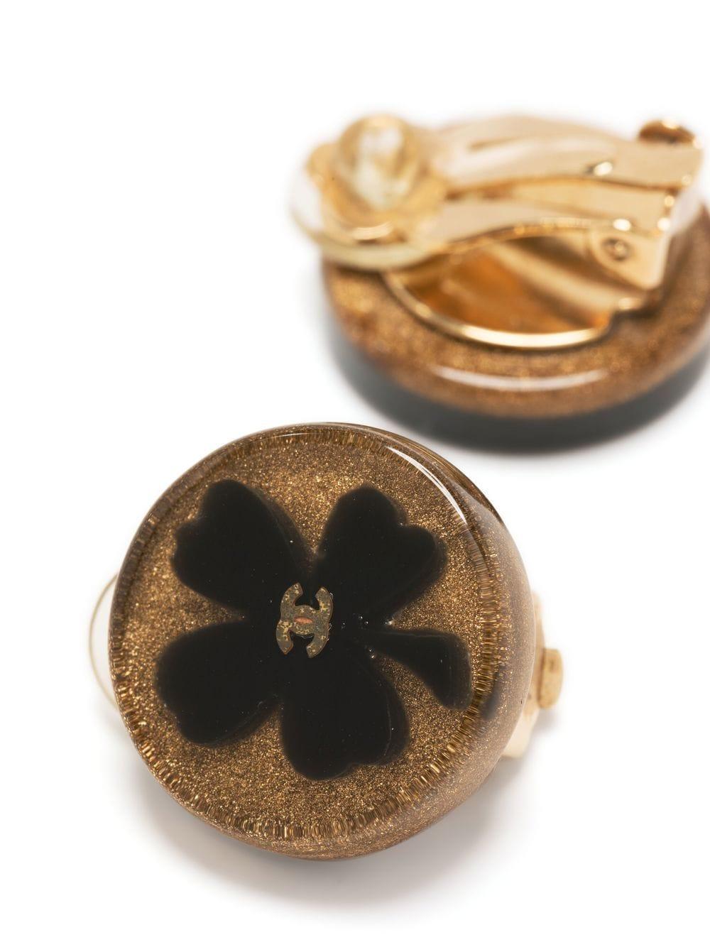 Schwarze Chanel-Klee-Clip-Ohrringe aus dem Jahr 2001 mit folgenden Eigenschaften: schwarzes Kleeblatt aus Harz, Clip-Verschluss, hintere Plakette mit entkerntem Chanel-Logo am Clip. 
Diese Ohrringe werden als Paar geliefert.
Ca. 2001
0,8 Zoll (2 cm)