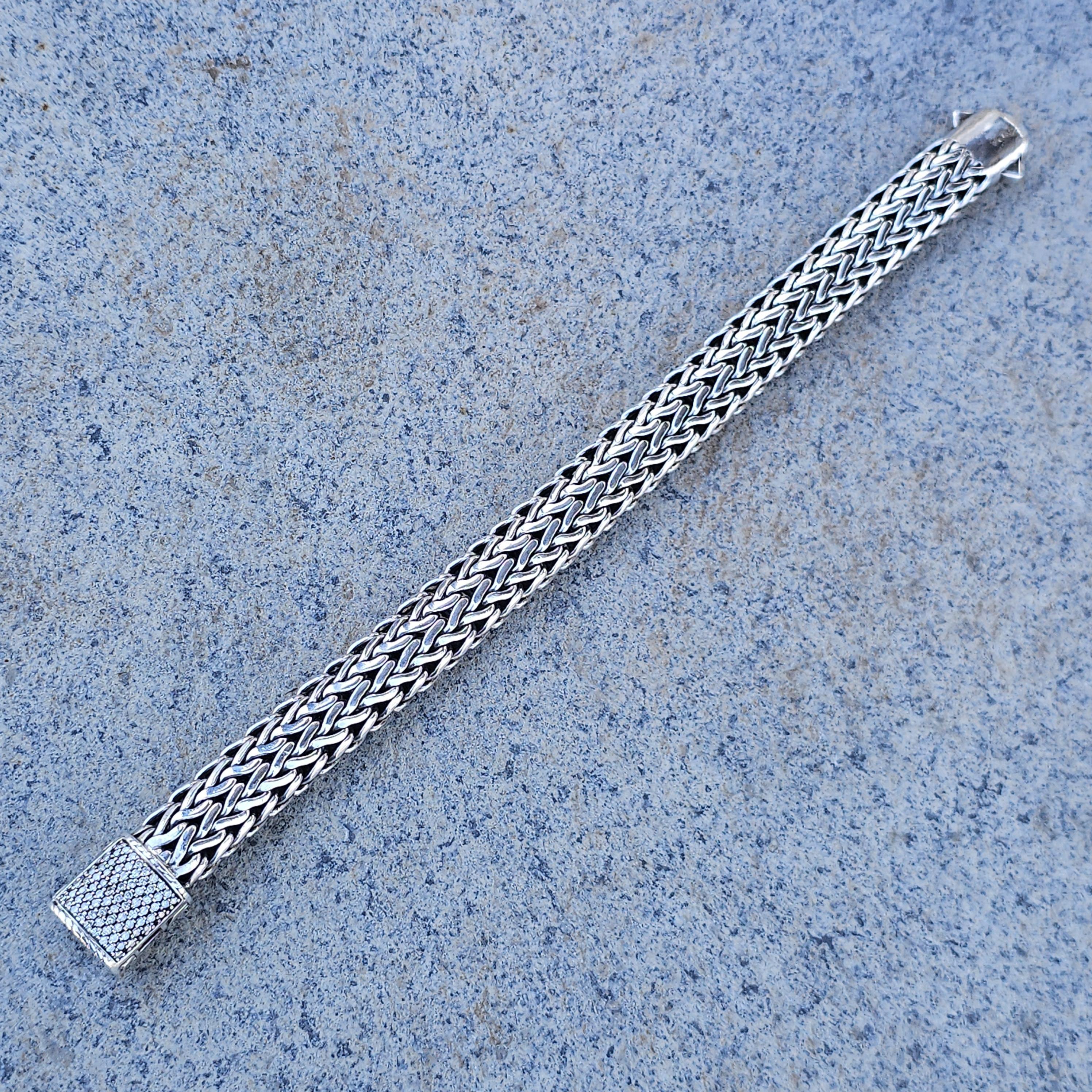 This John Hardy bracelet is a striking piece for any jewelry enthusiast. Crafted from sterling silver, it features a woven design with an 18k gold accent on back of clasp adorned with white pave diamonds. The intricate pattern adds a touch of