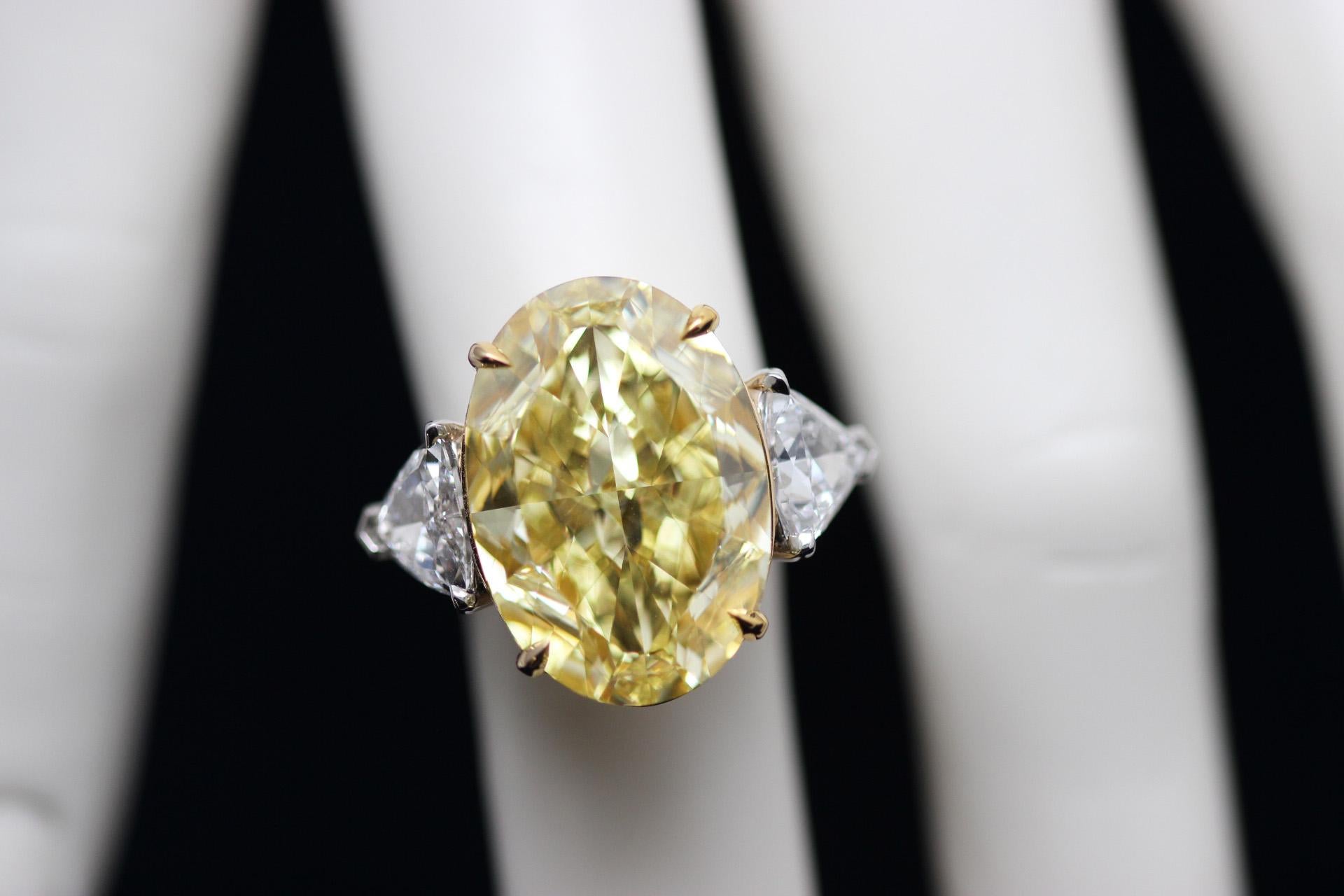 A modern classic from Scarselli  - a GIA-certified 20.02 carat Fancy intense yellow oval-cut diamond set in an 18k yellow gold basket with a platinum band. Two trapezoid-cut white diamonds (2.01 carats total) embellish the center stone, adding a bit