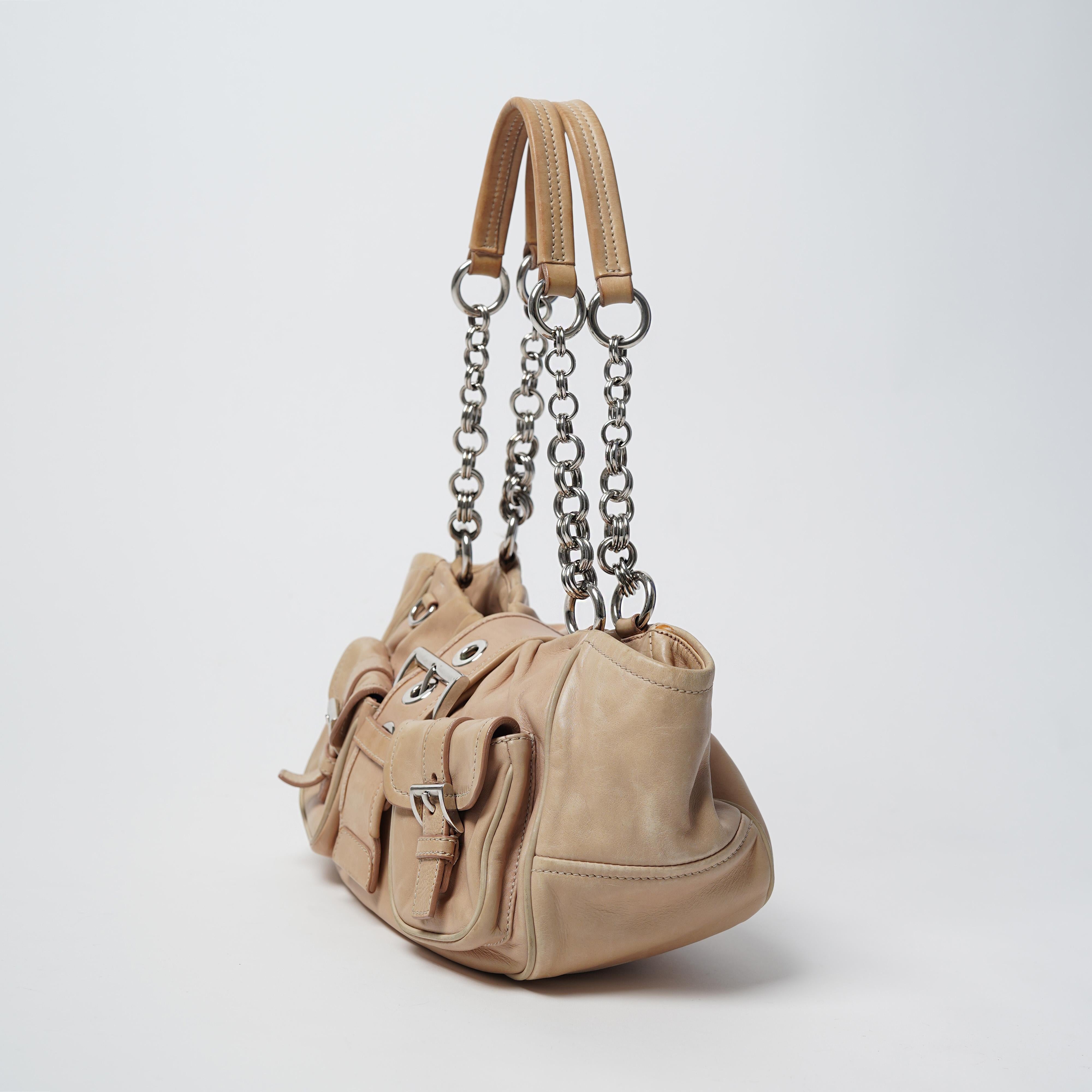 Presenting the 2002 Prada sand-toned leather moon bag with silver coloured chain strap and large center metal buckle. From its first iteration in the Spring/Summer 2002 collection the Prada Moon bag has since become a wardrobe staple in heavy