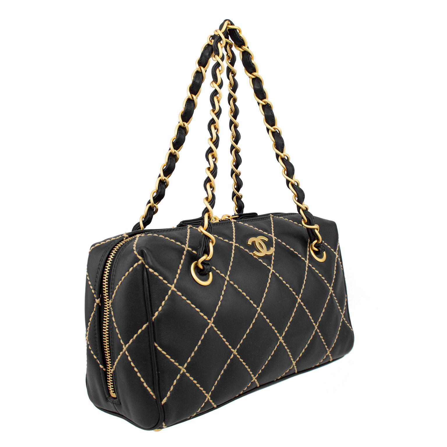 Designed in 2003 by Karl Lagerfeld for Chanel, this small Surpique bowler bag would be a wonderful addition to your collection. Supple black leather with beige quilted top stitching. Small gold tone metal interlocking cc logo. Gold chain and black