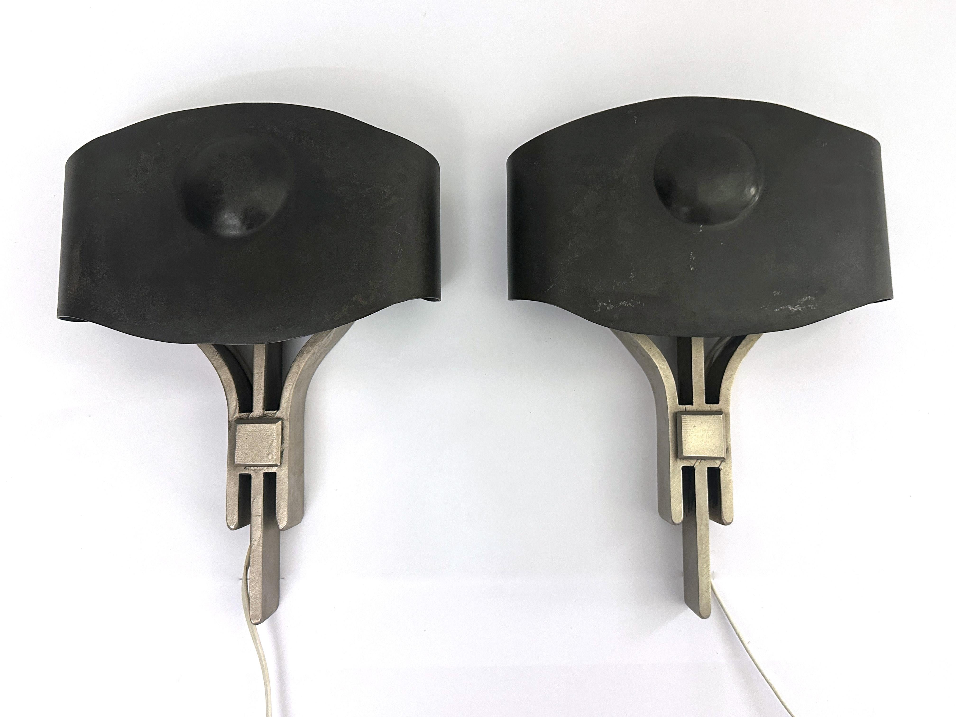 A pair of modern indutrial wall sconces deisign by Juan Montoya in 2003. This unique pair is made out of steel. Each body has a combination of brushed and patina steel to create contrast in the material. making a beautiful wall decorative piece when