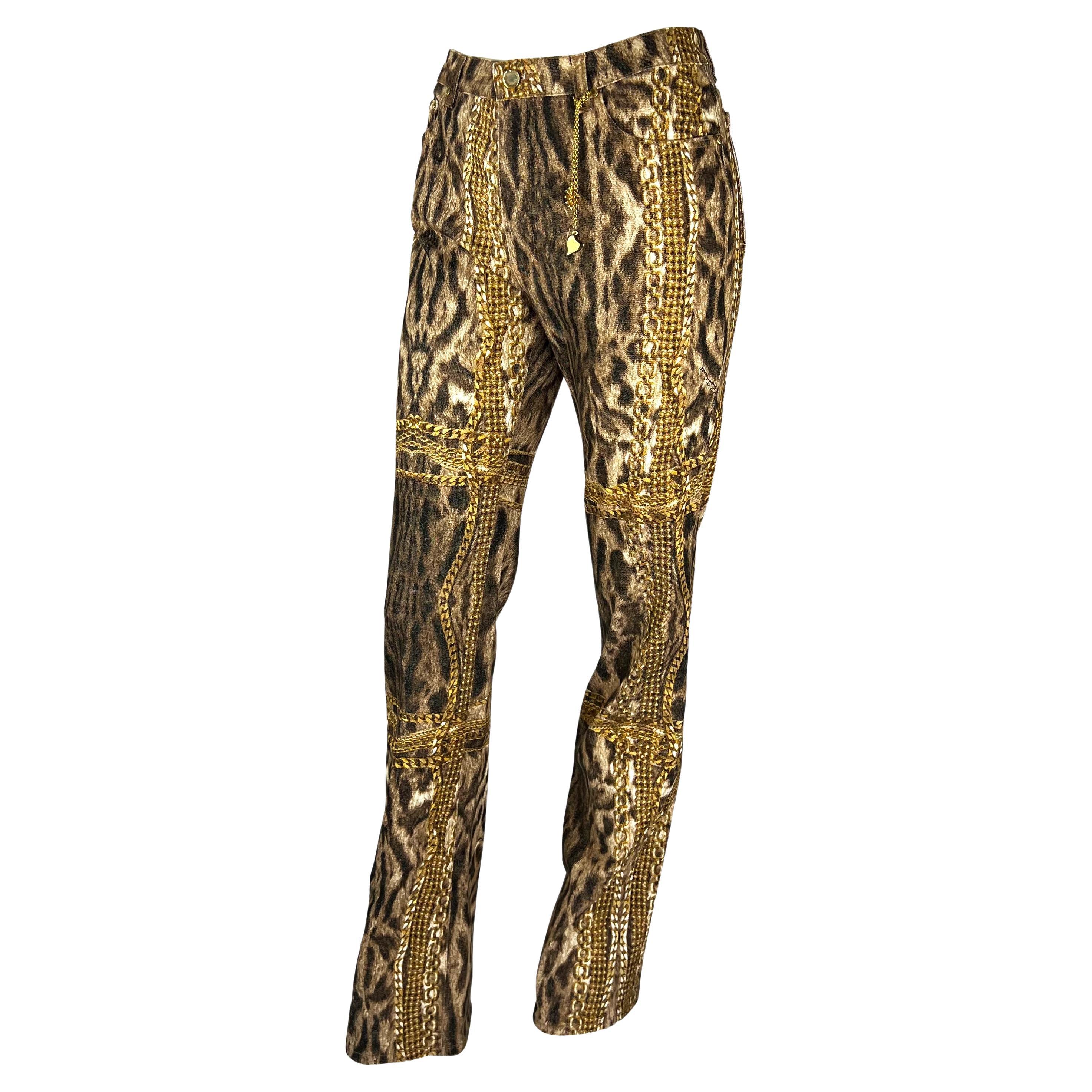 Présentation d'un pantalon en denim à imprimé guépard Roberto Cavalli. Datant de 2003, ce fabuleux pantalon présente un imprimé guépard et des chaînes dorées sur l'ensemble du corps. Ce pantalon est complété par une breloque en métal doré