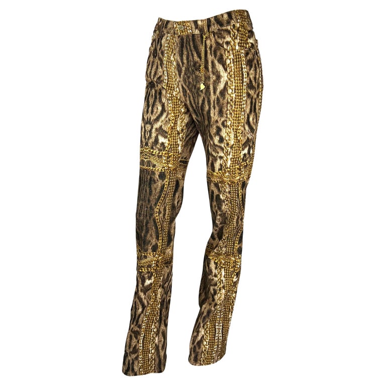 TheRealList presents: a pair of cheetah print denim Roberto Cavalli pants. From 2003, these fabulous pants feature a cheetah print with gold chains throughout. These pants are made complete with a metal gold-tone sun and heart charm at the front