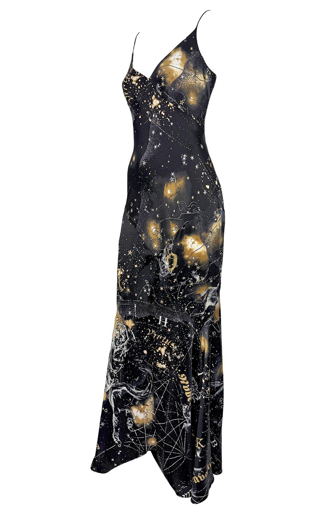 Dieses Abendkleid von Roberto Cavalli aus dem Jahr 2003 zeigt einen himmlischen Astrologie-Druck in Goldglitter auf schwarzem Seidensatin. Die schräg geschnittene Silhouette mit zarten Spaghettiträgern, tiefem Dekolleté und leicht ausgestelltem Saum