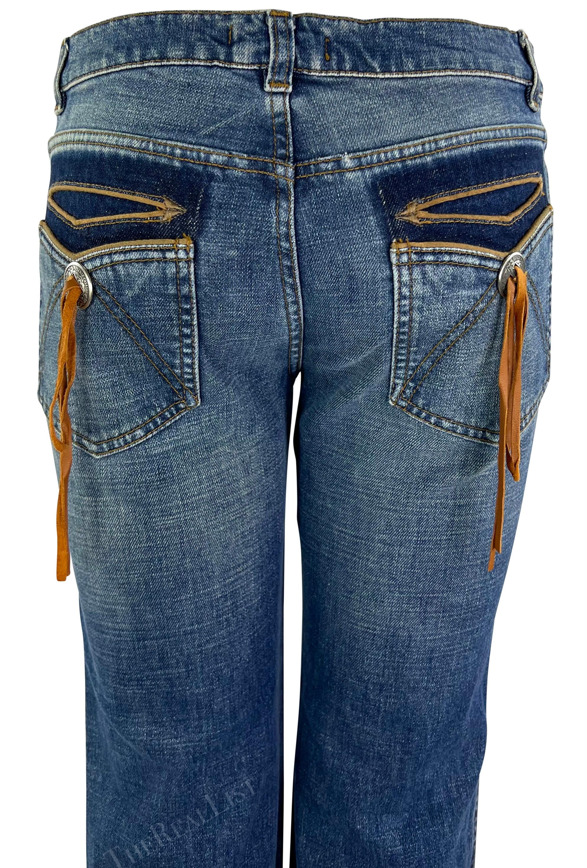Ich präsentiere eine Jeans von Roberto Cavalli in heller Waschung. Diese leicht ausgestellte Jeans aus dem Jahr 2003 ist mit einem silberfarbenen Metallknopf und Wildlederfransen an den Gesäßtaschen verziert. Diese vom amerikanischen Westen