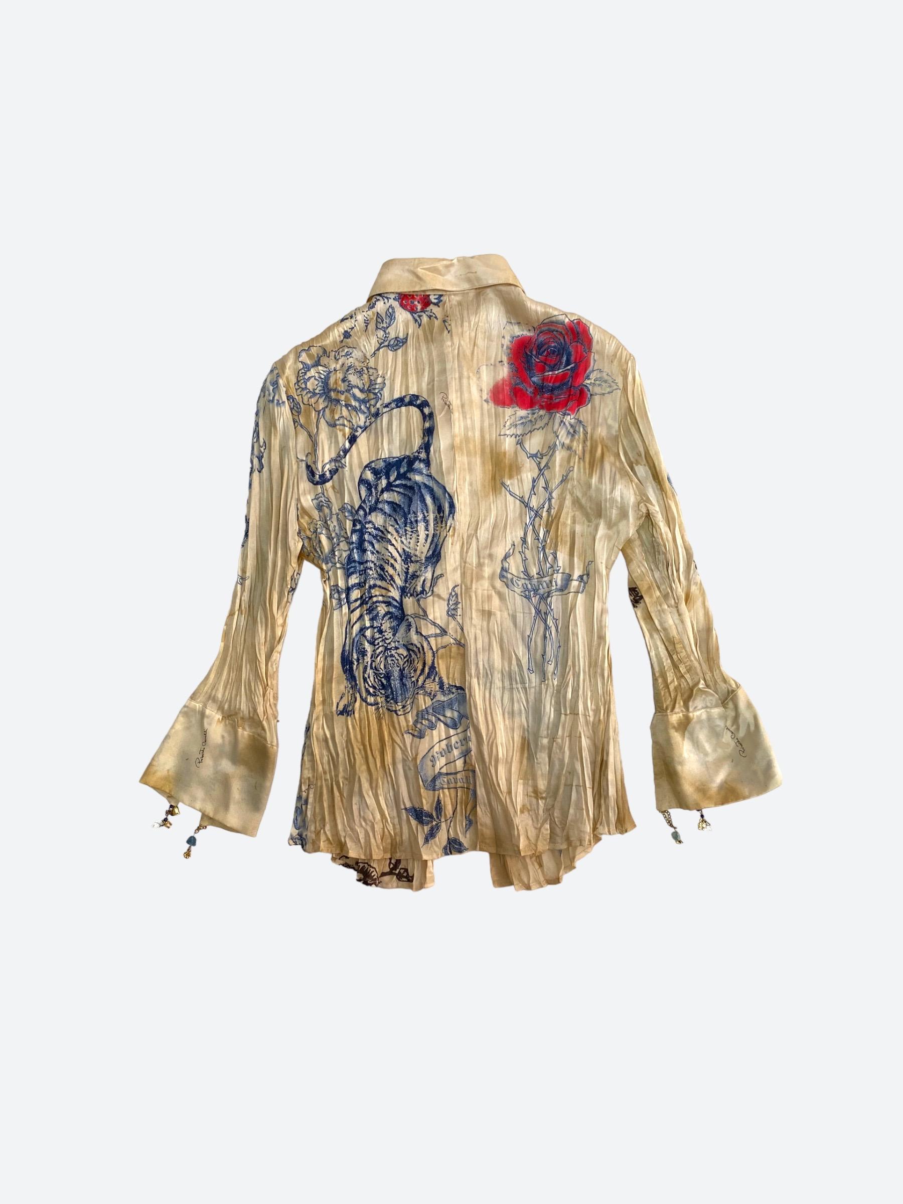 This golden-toned, 100% silk shirt displays a blue and red graphic chinoiserie print that resembles tattoos, along with delicate jewel embellishments on the cuffs. 

The darker toned areas and Cavalli-signature creased finish of the silk fabric