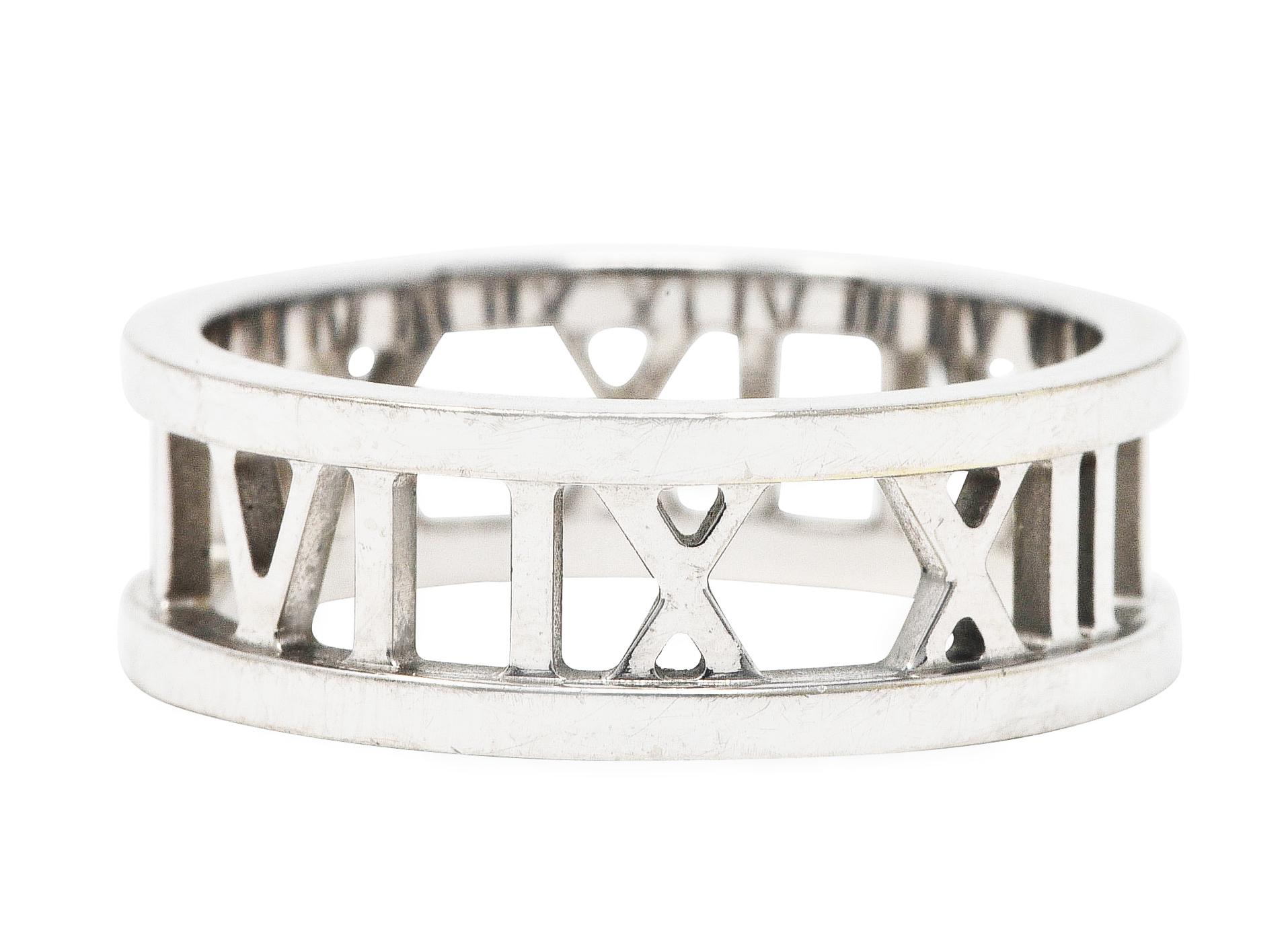 Band ring is pierced with Roman numerals fully around

Motif is flanked North to South by raised and polished edges

Stamped 750 for 18 karat white gold

Fully signed 2003 Tiffany & Co.

From the Atlas collection

Ring size: 7 1/2 and not