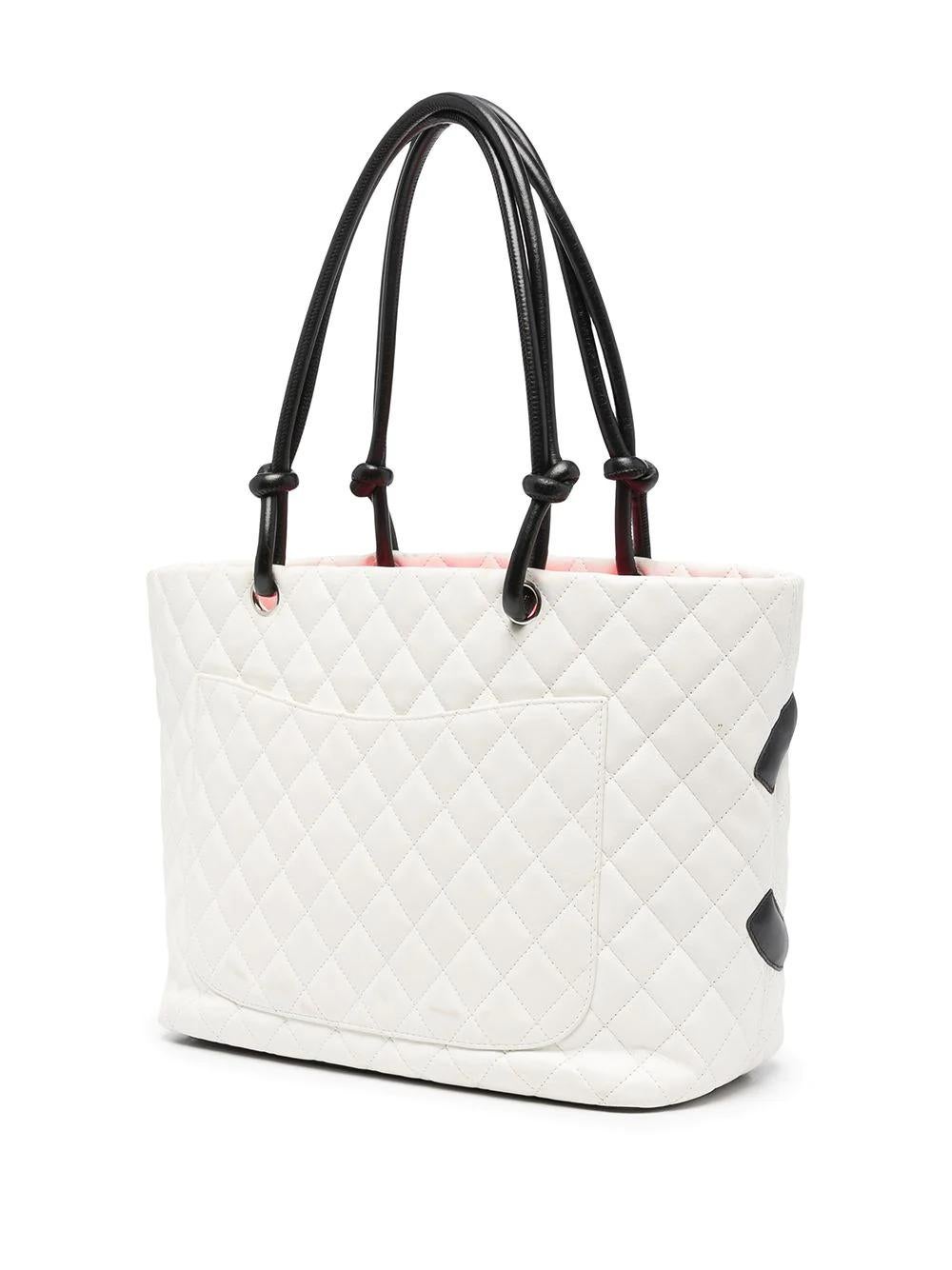 From the 2004-2005 Cambon Collection, this pre-owned Chanel tote bag is crafted from white quilted leather and displays a bold interlocking black CC logo. It features an exterior back slip pocket, dual-rolled black leather handles with knotted ends