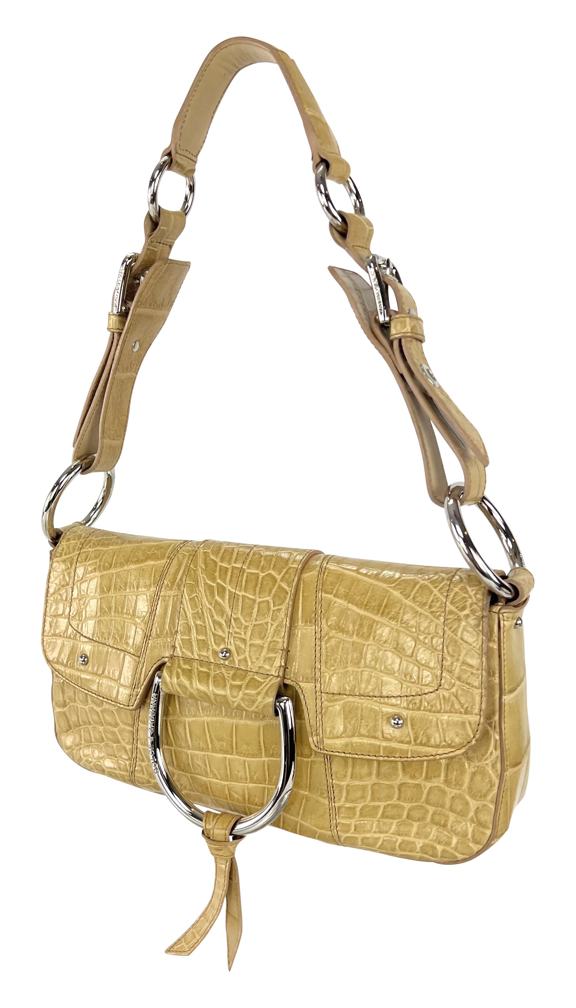 This 2004 Dolce & Gabbana shoulder bag is crafted from tan genuine crocodile leather, featuring a structured flap design with large silver-tone metal rings and a front D-ring detail. The bag has magnetic closures and an adjustable shoulder strap