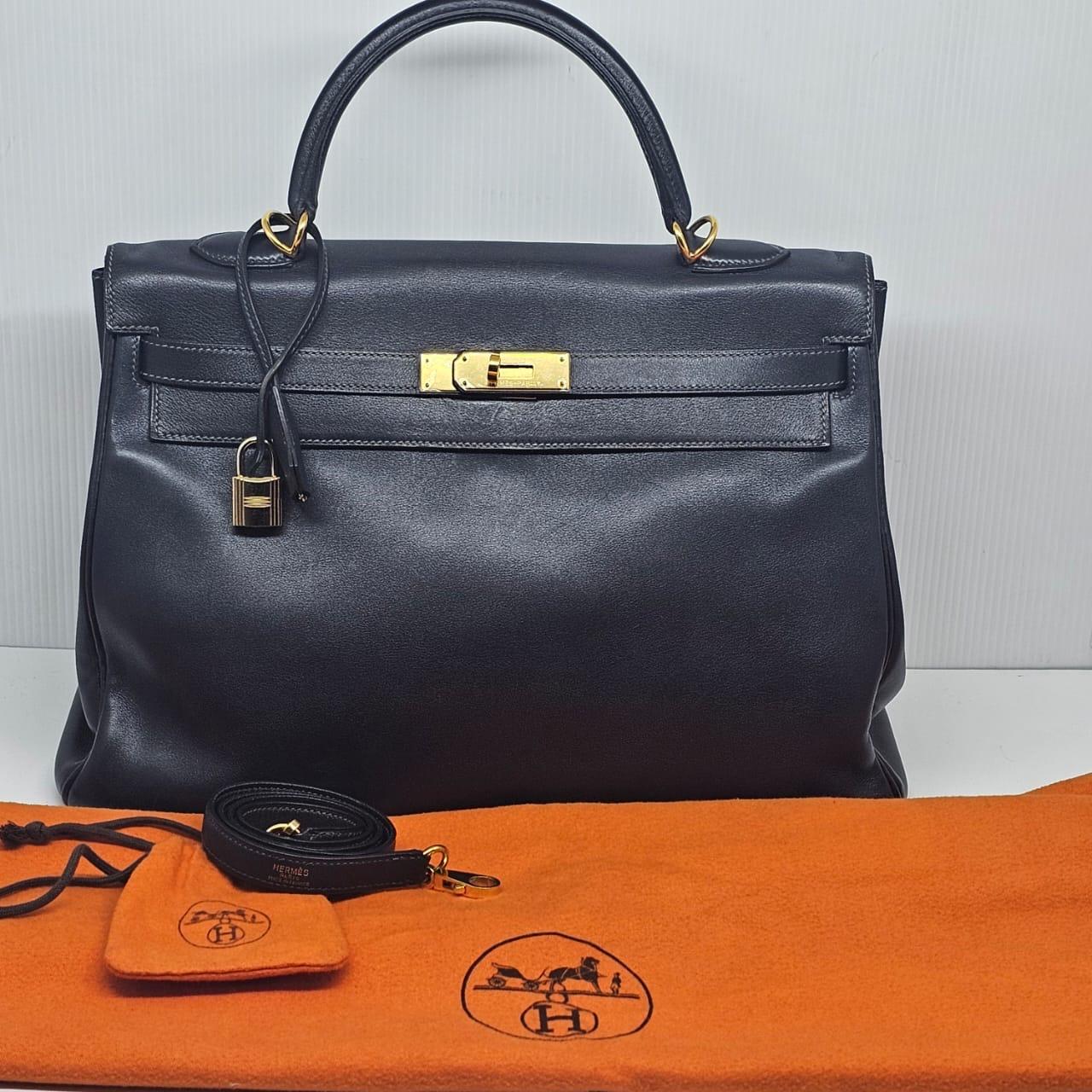 Kelly Clásica 35 en piel Swift azul índigo con herrajes dorados. Ligeros arañazos y pérdida de estructura en el cuerpo de la bolsa, pero en general sigue en buen estado. Se entrega con su correa, bolsa guardapolvo, llaves y candado. Sello cuadrado H