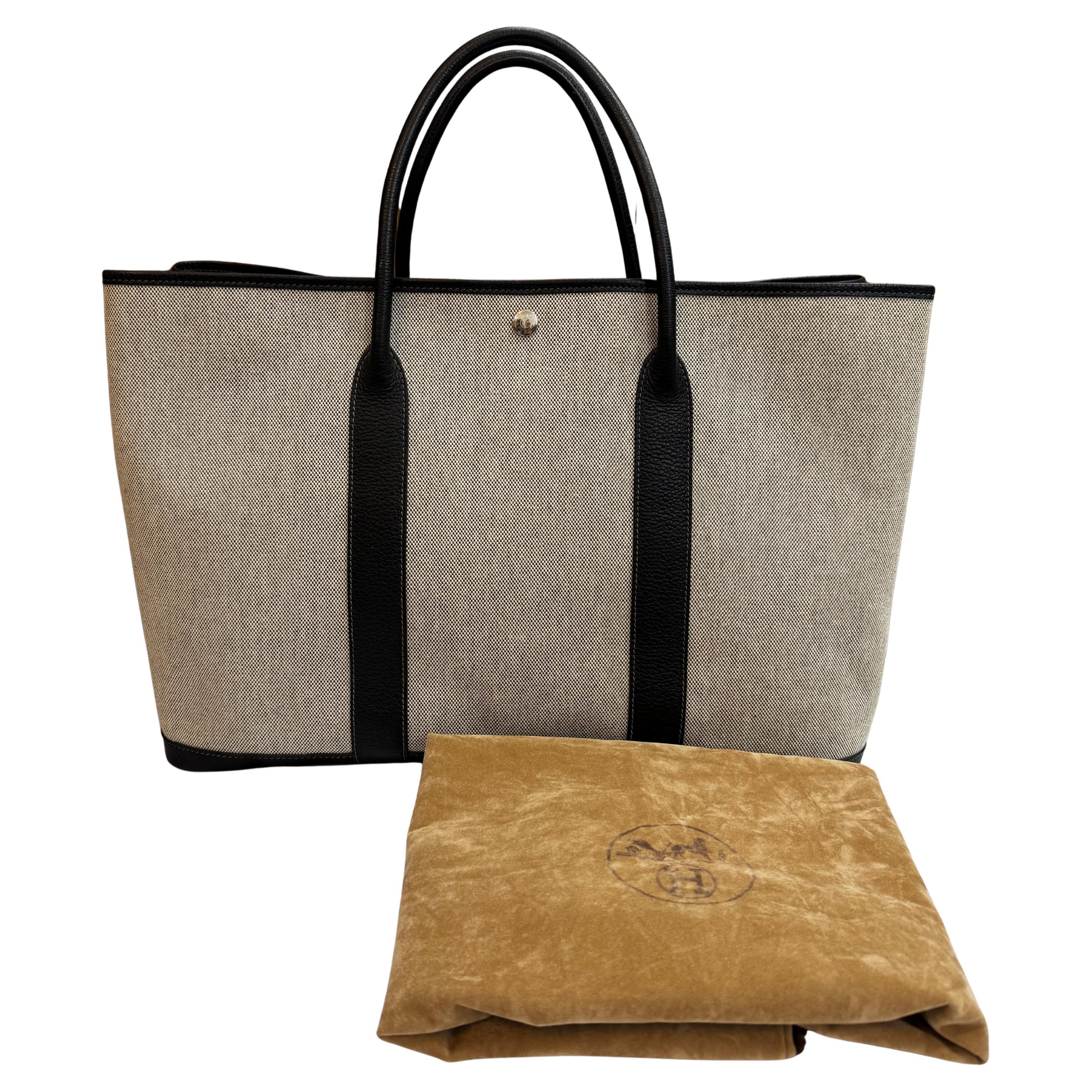 Ce sac fourre-tout vintage HERMES MM Garden Party est réalisé en toile grise garnie de cuir de veau à gros grain noir, avec des ferrures en palladium et des anses en cuir roulé. L'ouverture large sur le dessus avec fermeture à bouton-pression donne