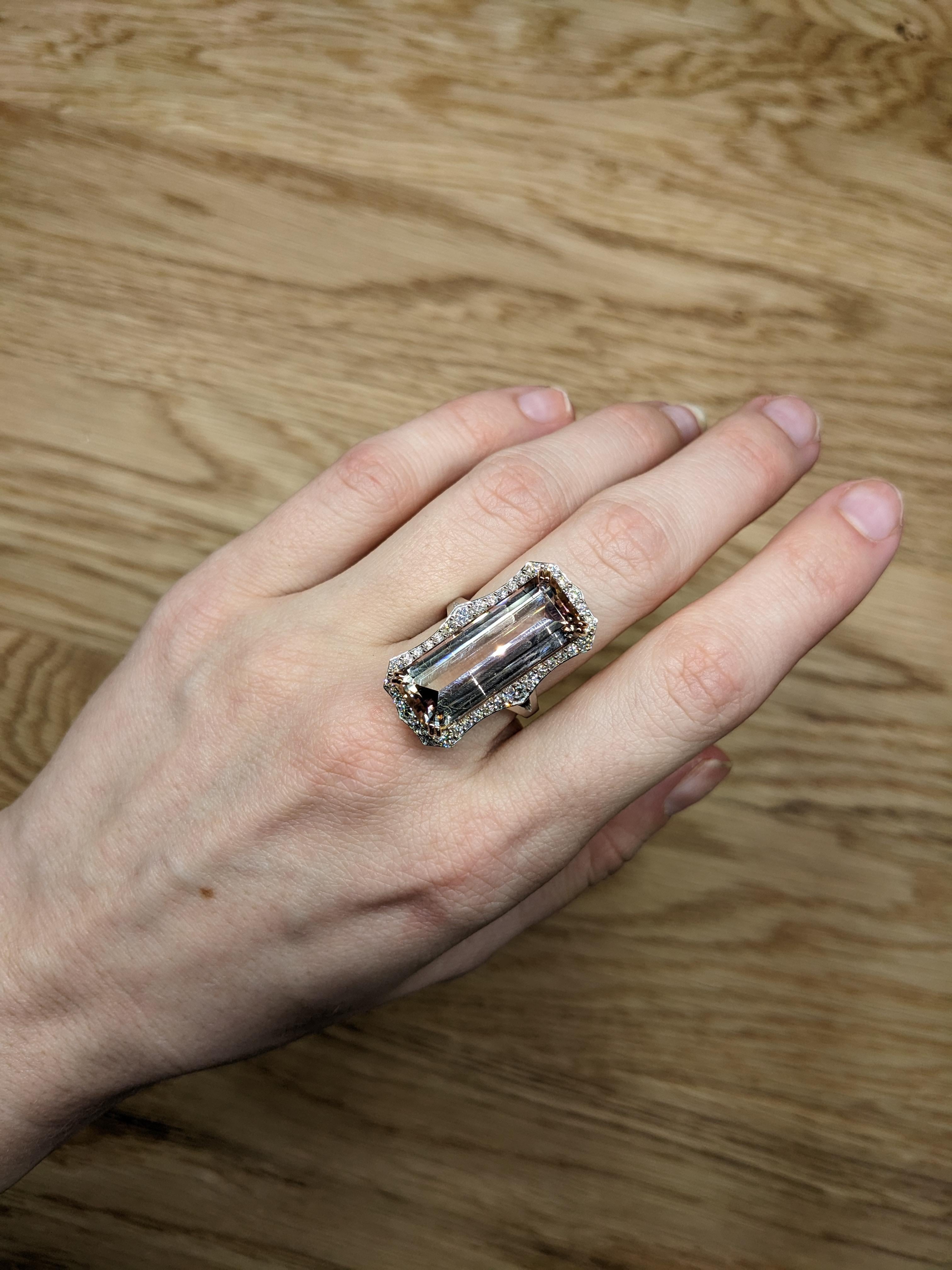 A stunning ring showcases a dazzling 20.04-carat pink tourmaline in an elegant emerald cut, measuring 25x10mm. The vibrant pink hue of the tourmaline is expertly framed by a delicate halo of shimmering diamonds, enhancing its brilliance and giving