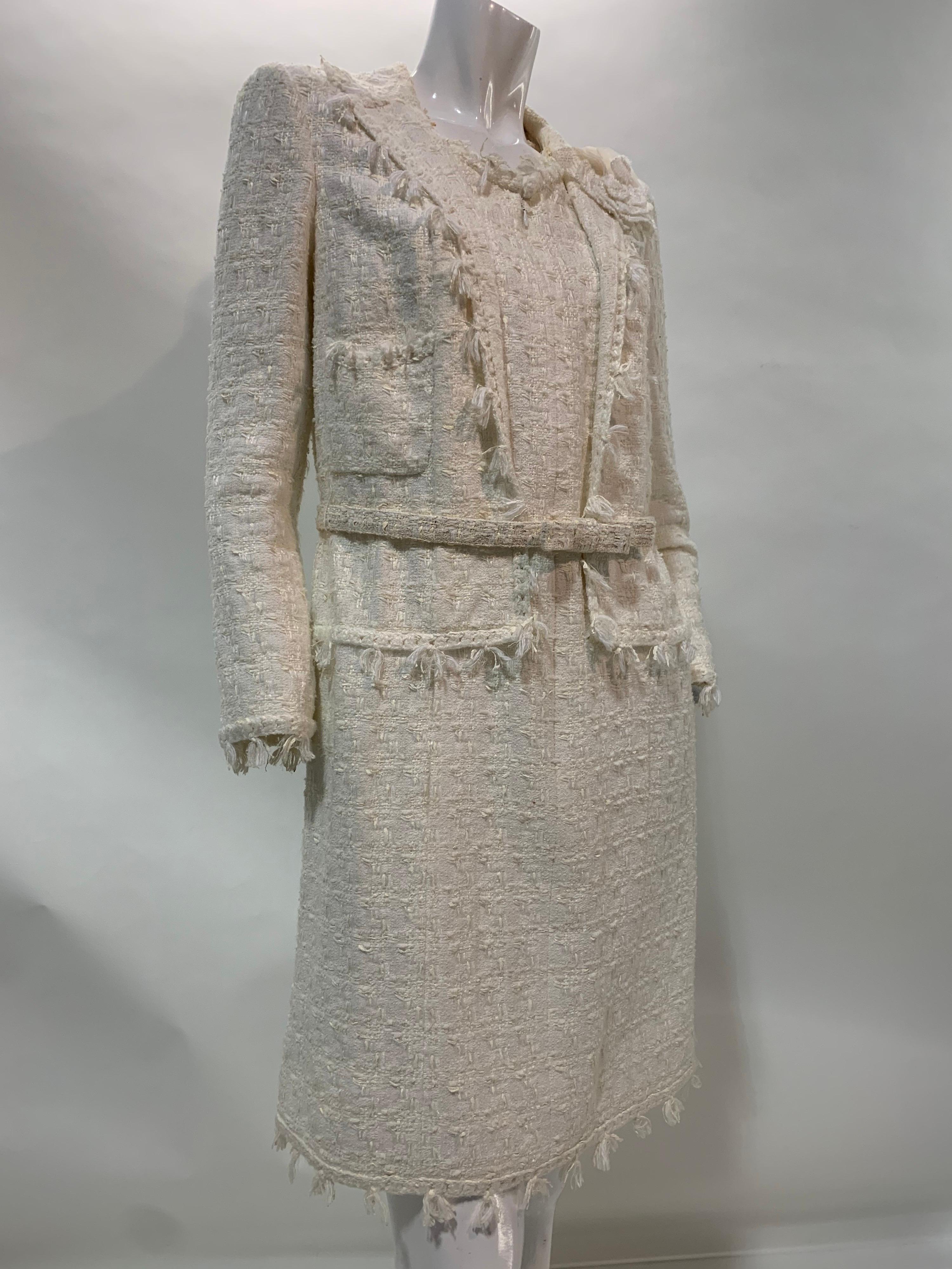 2005 Chanel ivory multi-fiber blend boucle weave coat dress in a tailored silhouette with front zippered closure and tuft fringe detail. Attached faux jacket with silver-tone camellia buttons. Matching original structured bow belt and detachable