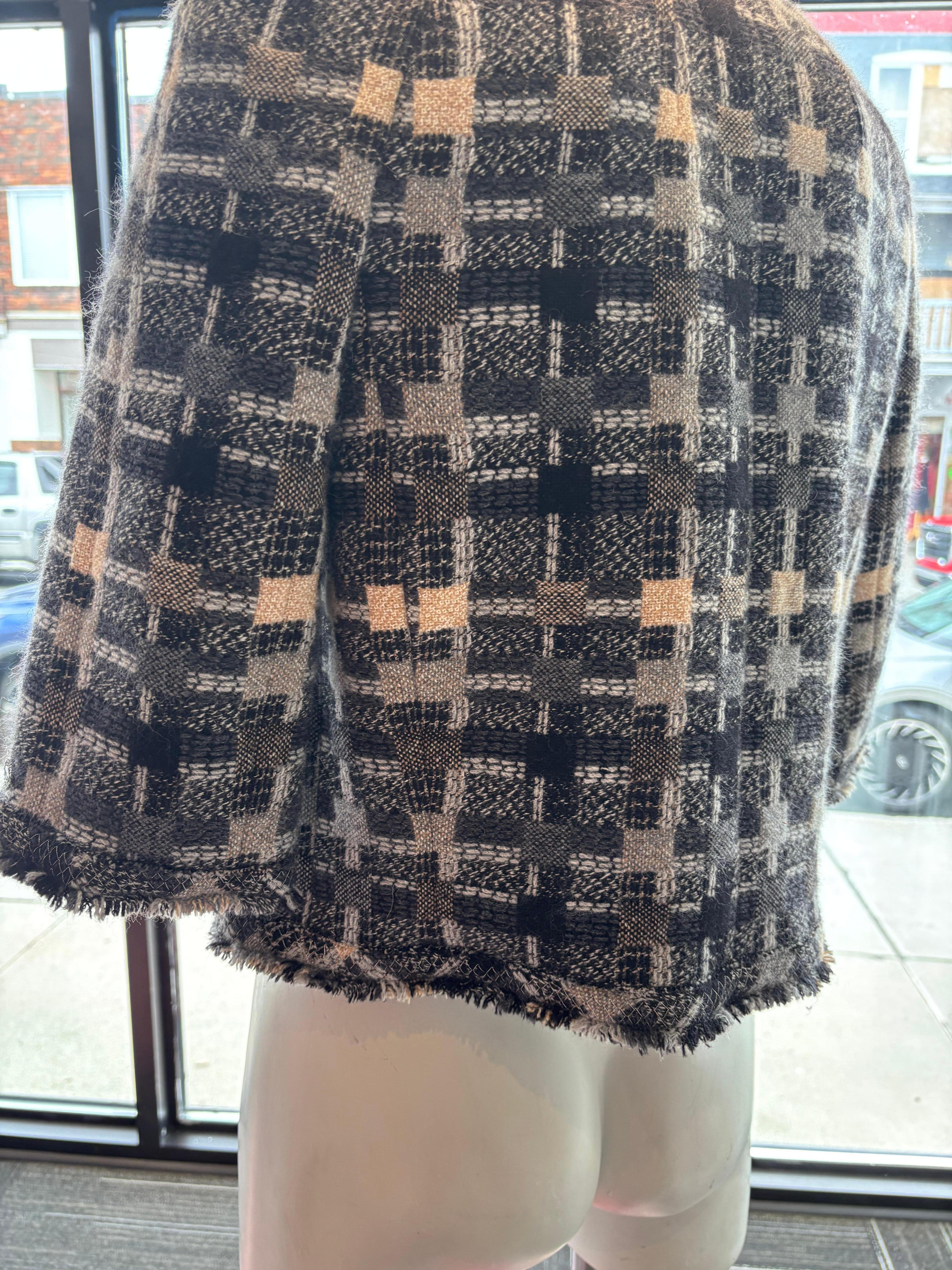 This vintage Chanel jacket is a tweed check pattern in grey, black and beige.
The jacket has 3/4 sleeves; round collar; raw edges; the chain at the hem; an oblong  Chanel plaque om the left sleeve cuff; patch pockets; silk CC logo lining, and silver